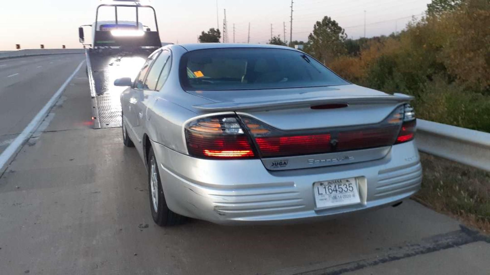 A silver Pontiac Grand Prix parked on a highway shoulder behind a tow truck.