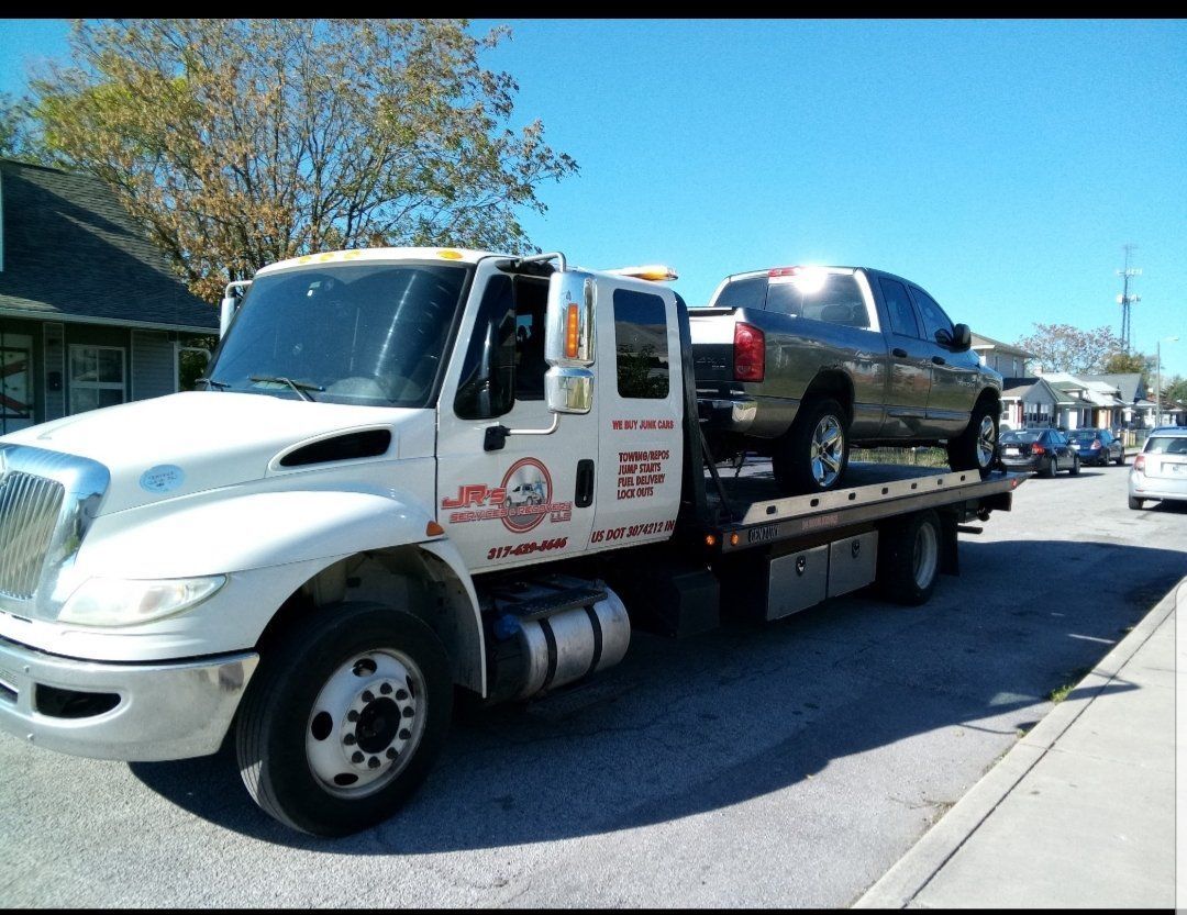 A white tow truck transporting a gray pickup truck parked on a sunny residential street.