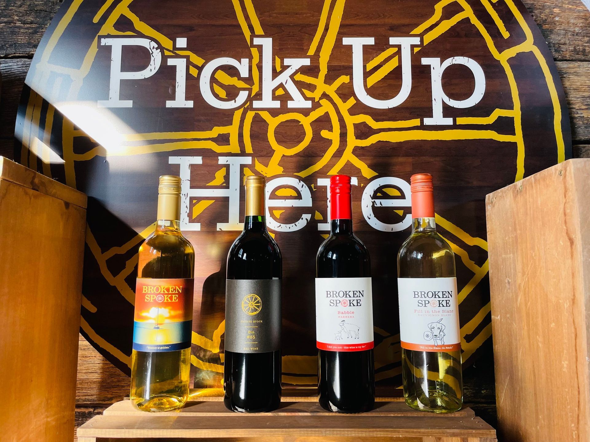 Four bottles of wine are displayed in front of a sign that says pick up here