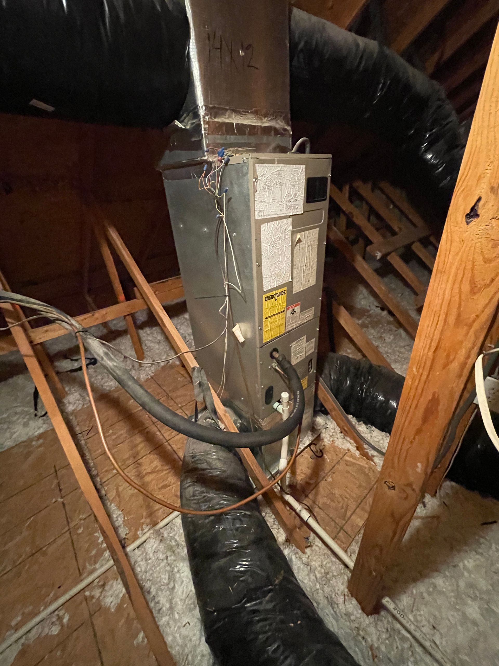 An air conditioner is hanging from the ceiling of an attic.