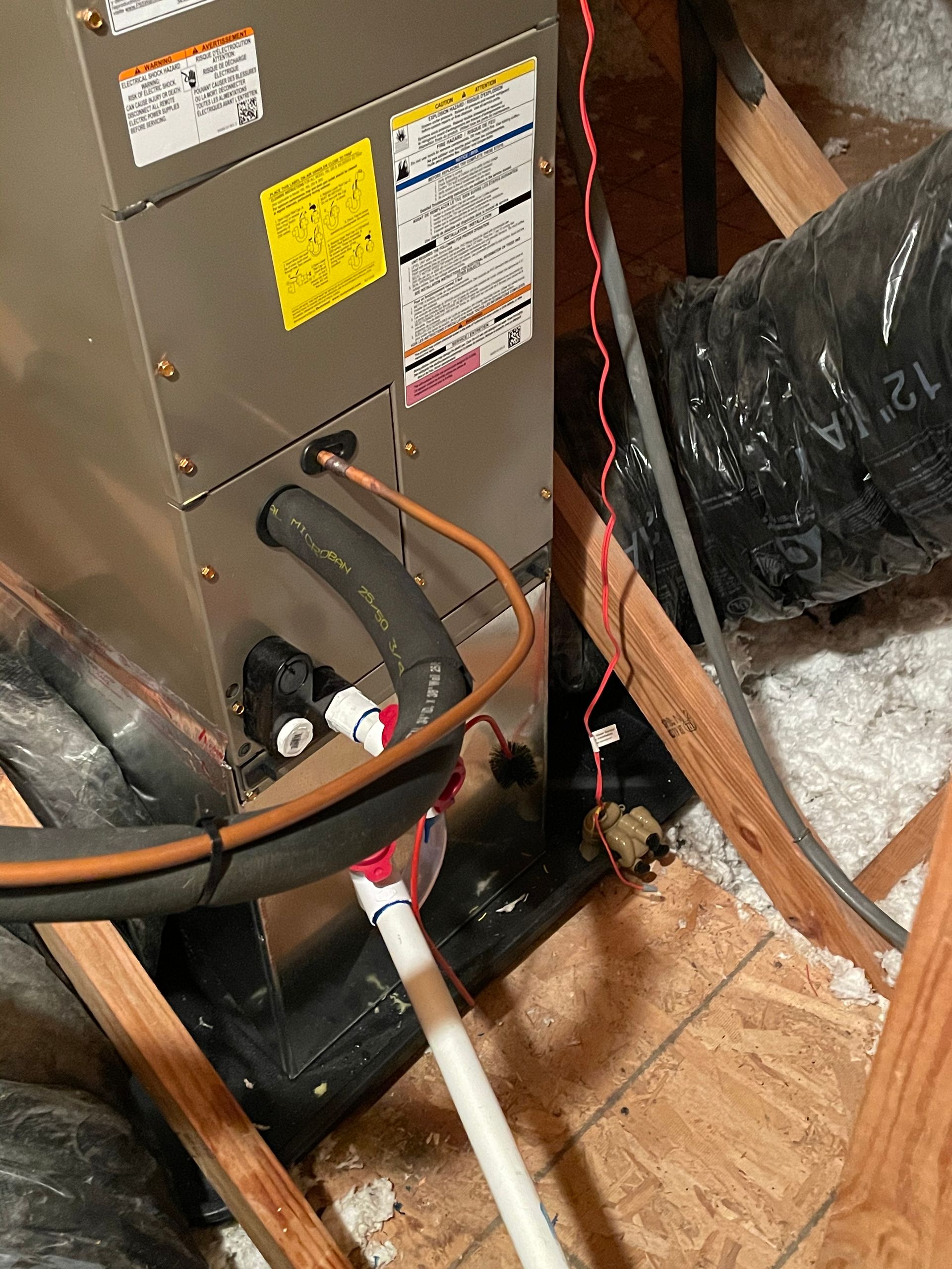 A close up of an air conditioner in an attic with pipes coming out of it.