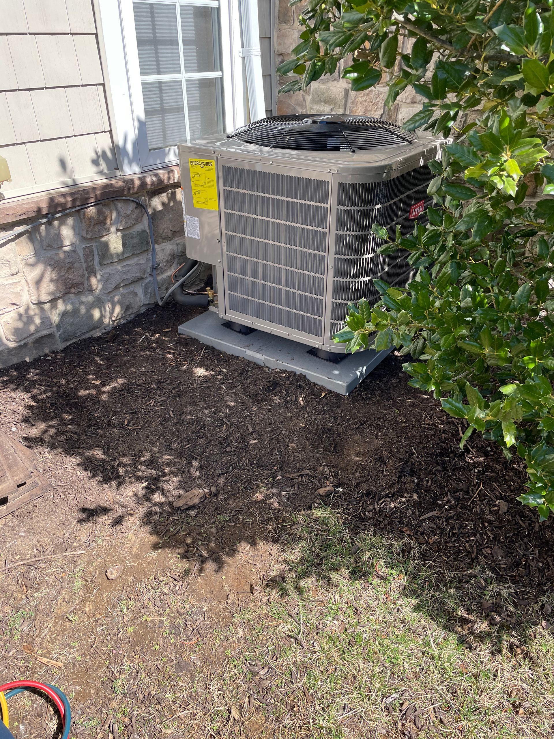 An air conditioner is sitting in the dirt in front of a house.