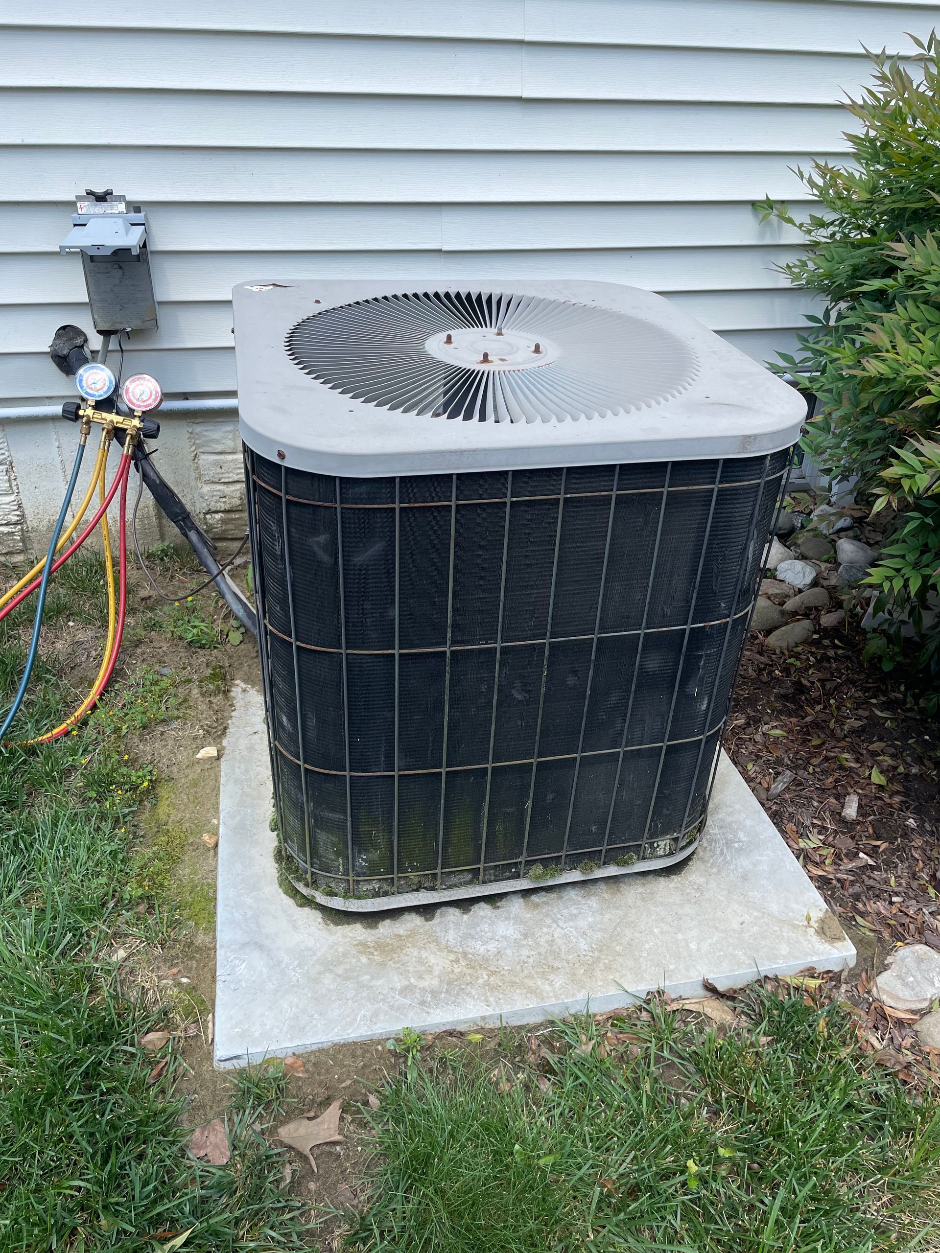 A black air conditioner is sitting on top of a concrete base next to a house.