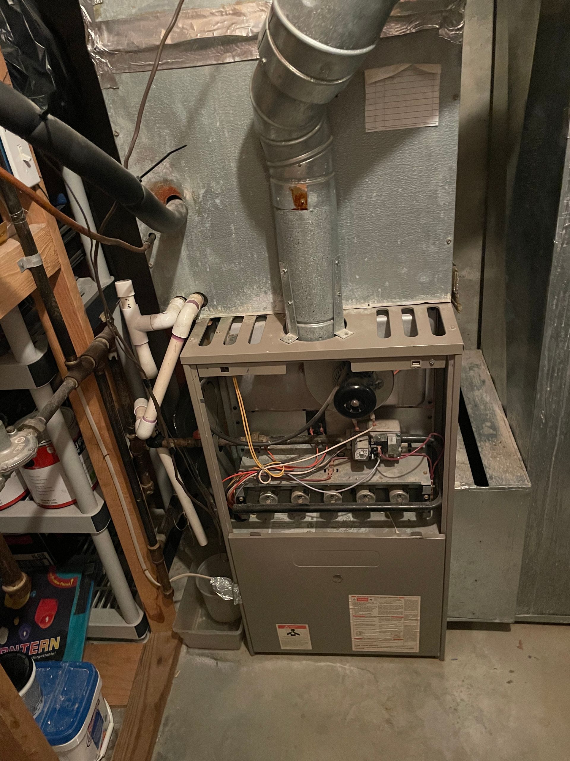 A furnace is sitting in a basement next to a ladder.