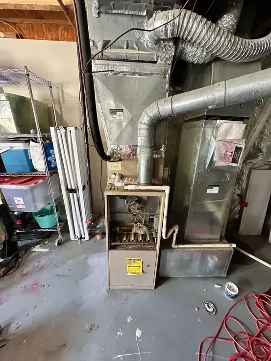 An air conditioner is sitting in a garage next to a hose.