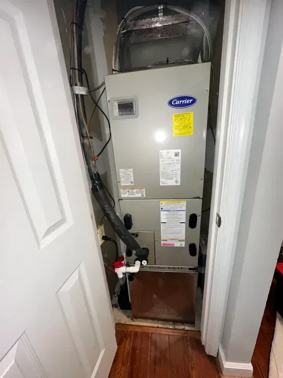 A carrier air conditioner is sitting in a closet next to a door.