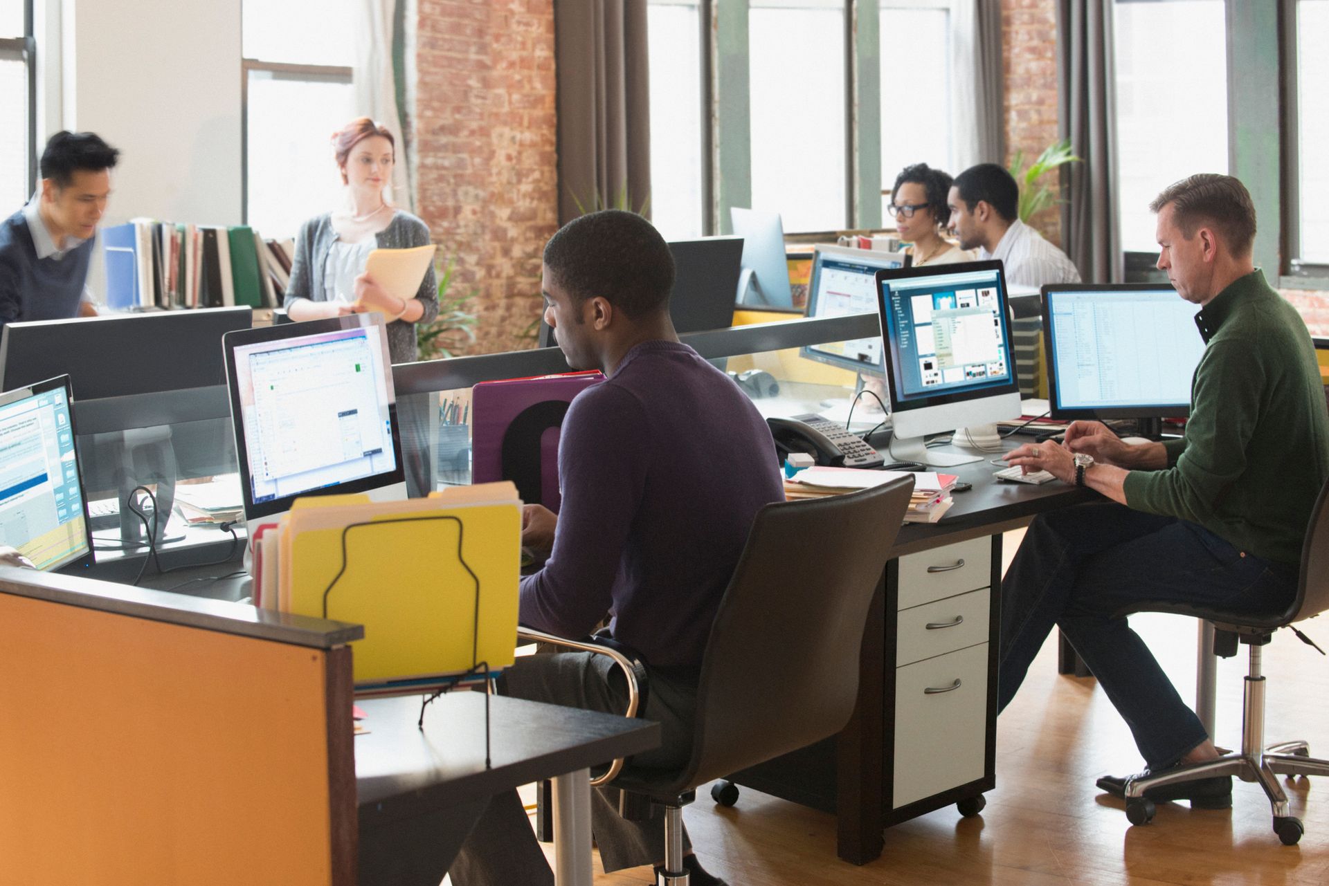 A group of people are sitting at desks in an office working on computers.