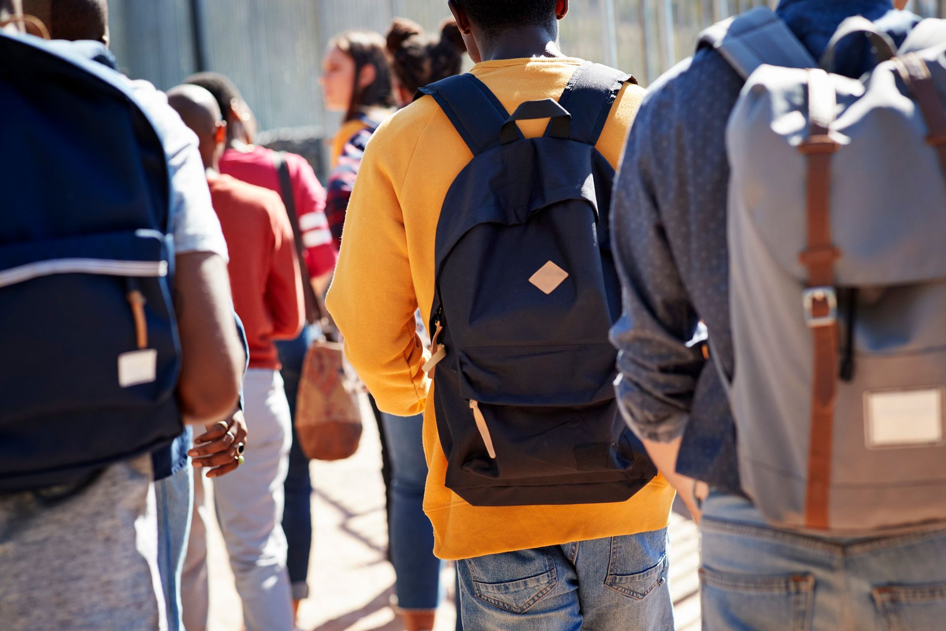 A group of people with backpacks are walking down a sidewalk.