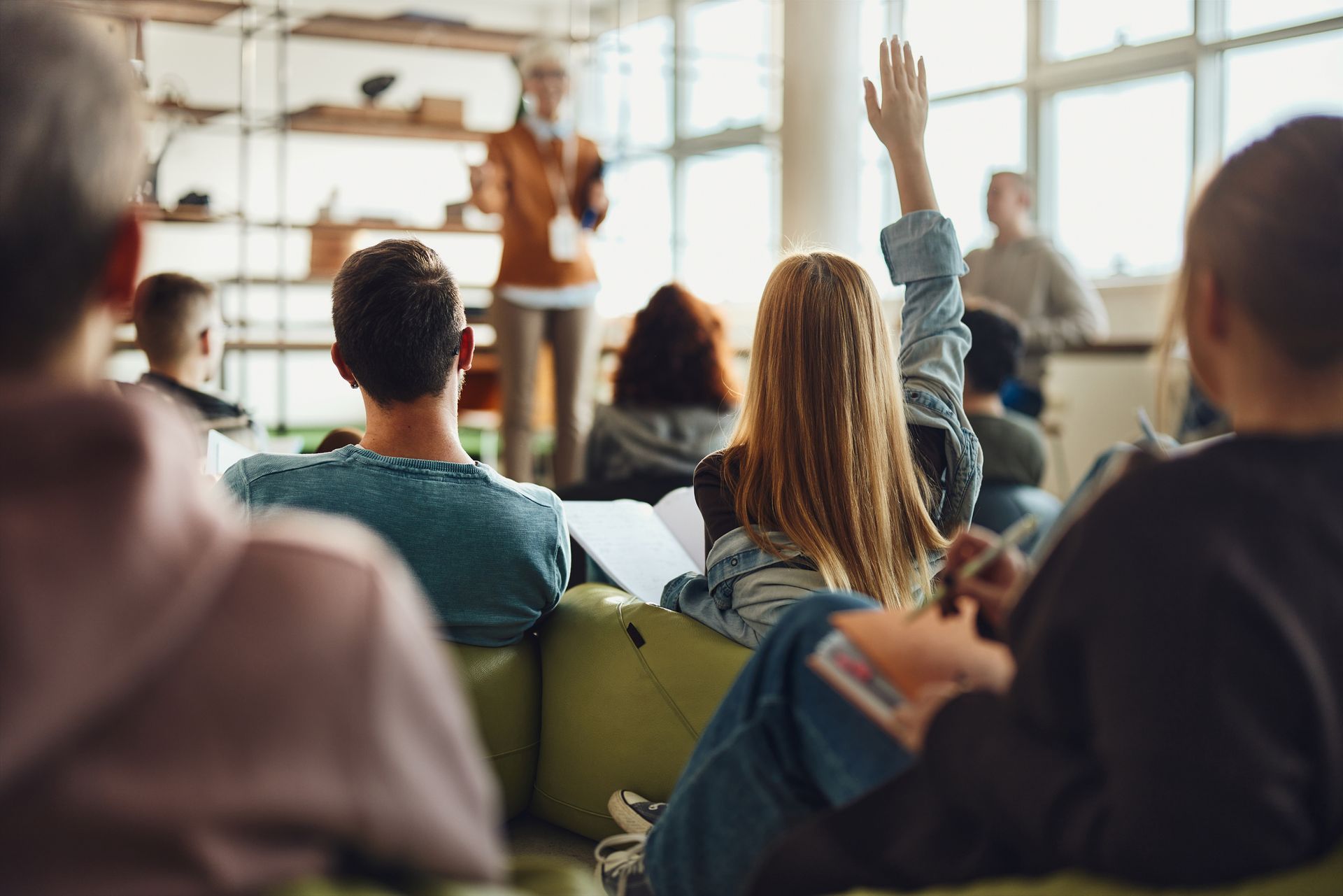 A group of people are sitting in a classroom raising their hands to answer a question.