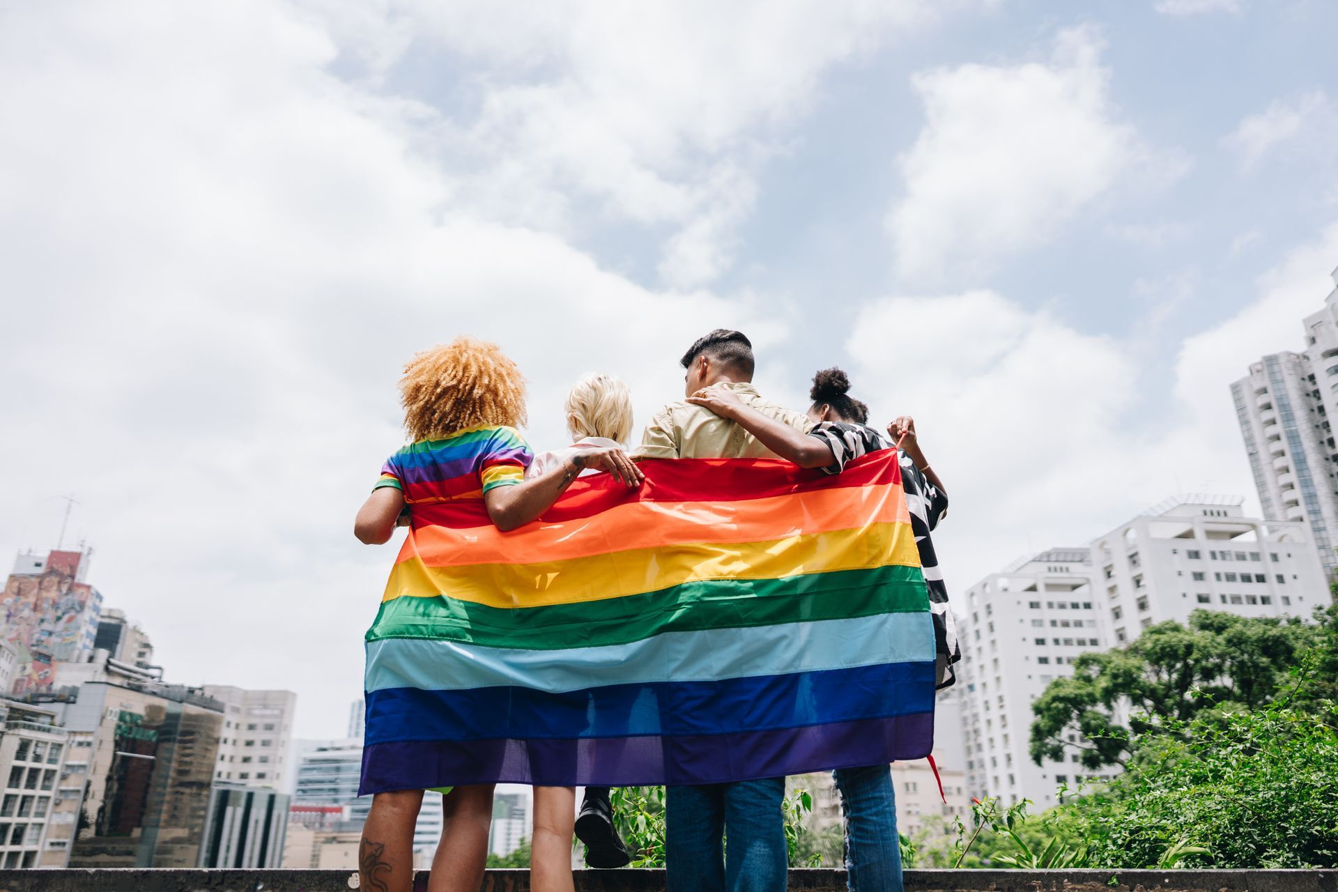 A group of people are standing next to each other holding a rainbow flag.