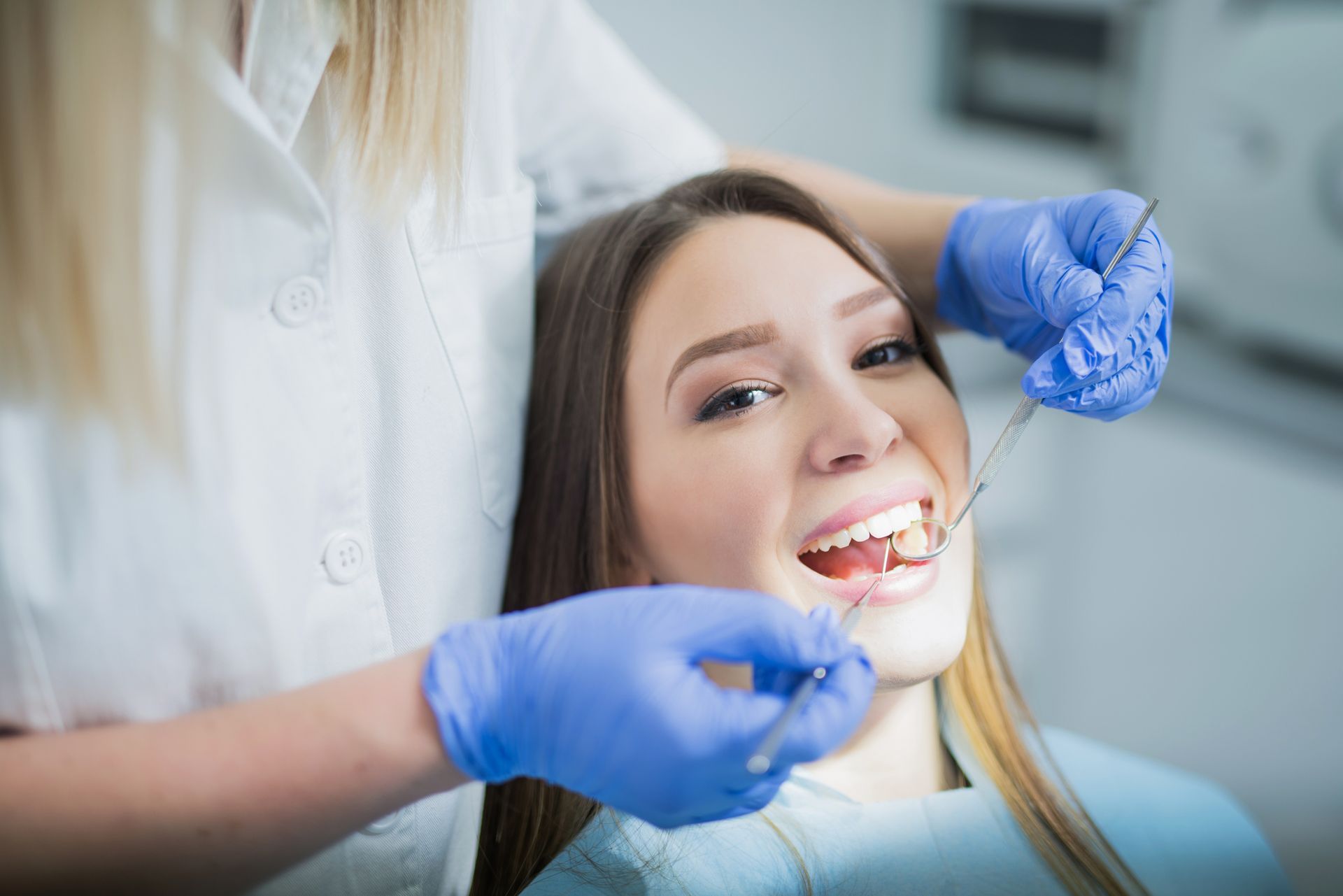 A woman is sitting in a dental chair while a dentist examines her teeth.