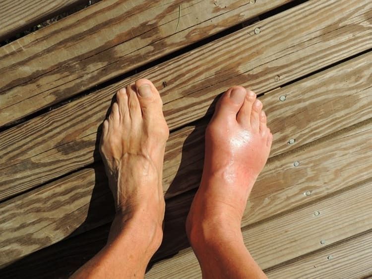 A person 's feet are standing on a wooden deck.