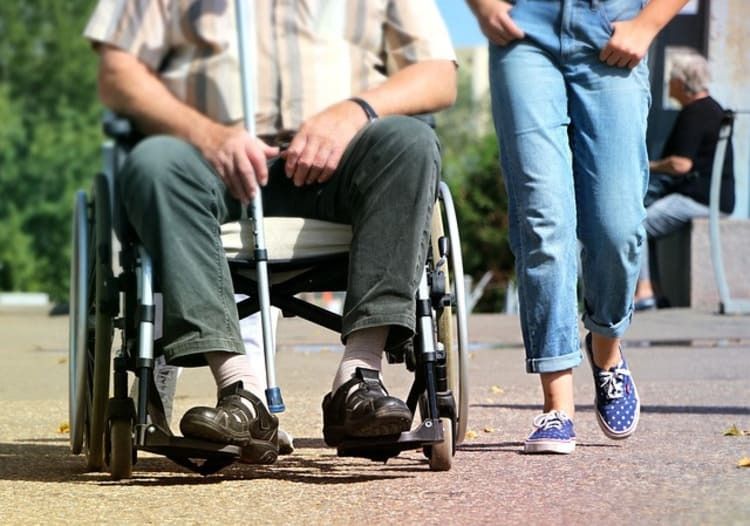 A woman is walking next to a man in a wheelchair.