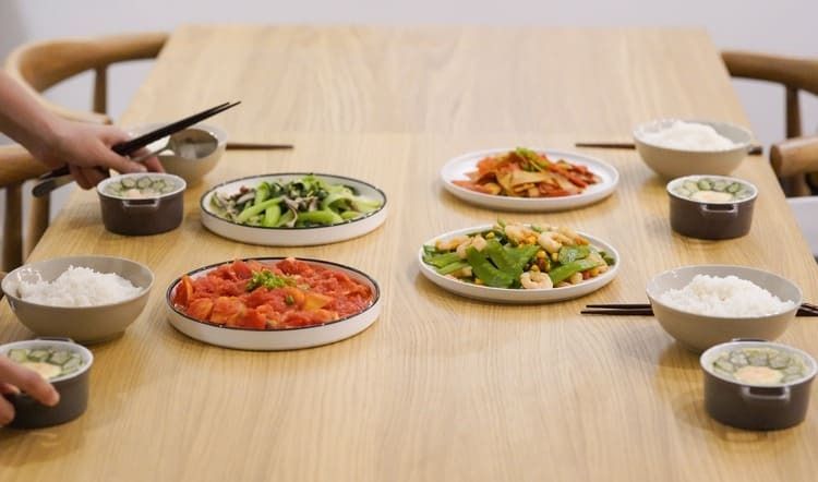 A wooden table topped with plates of food and bowls of rice.