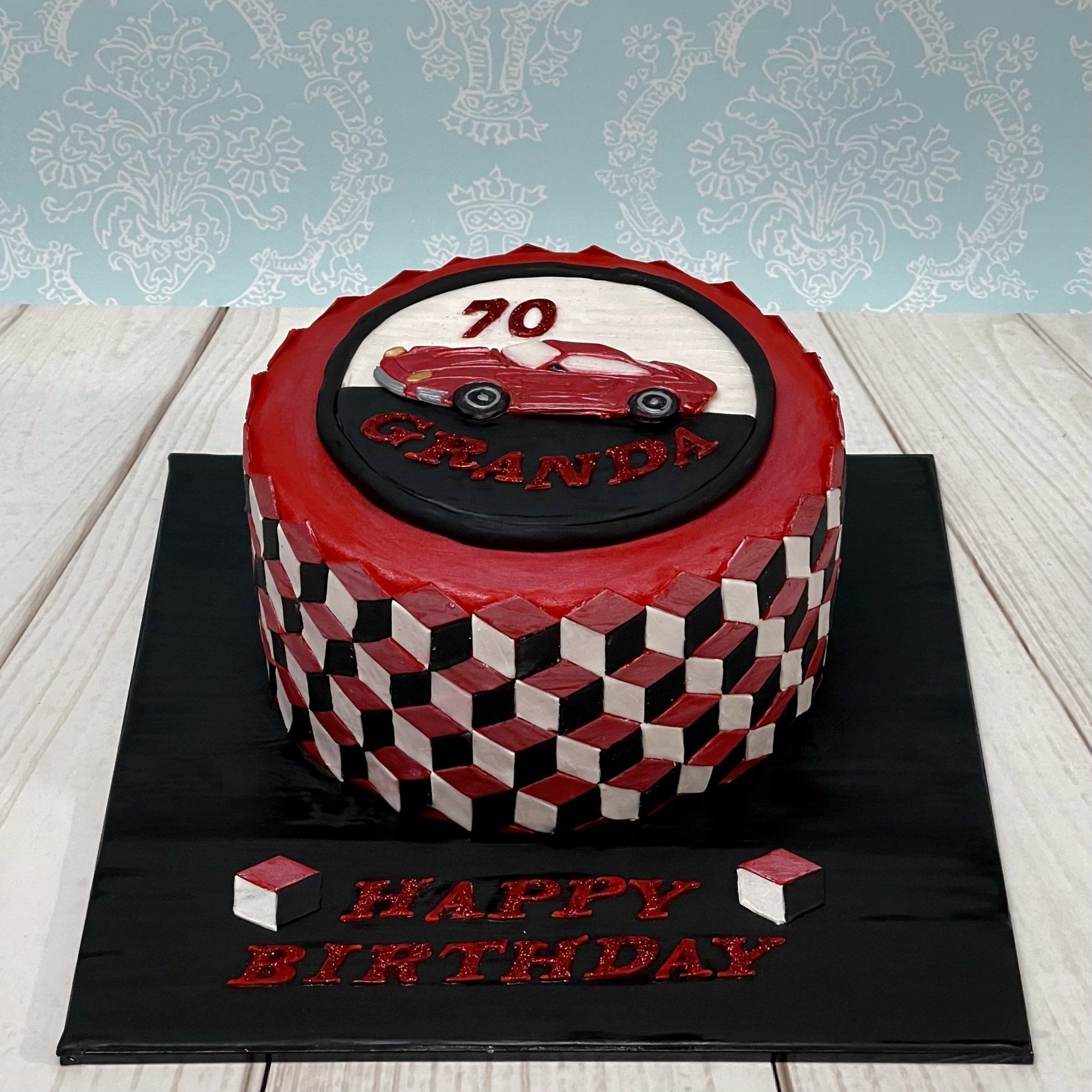 Birthday Cake with red patchwork sports car on the top and an optical illusions design around the base in red black and white.