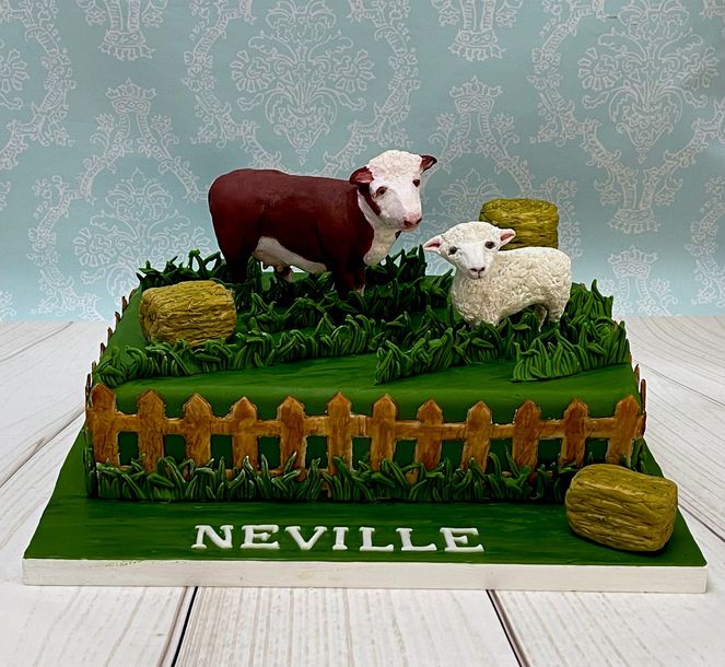Farm themed cake with hand sculpted fondant sheep, fondant cow, fondant grass and fondant bales of hay.