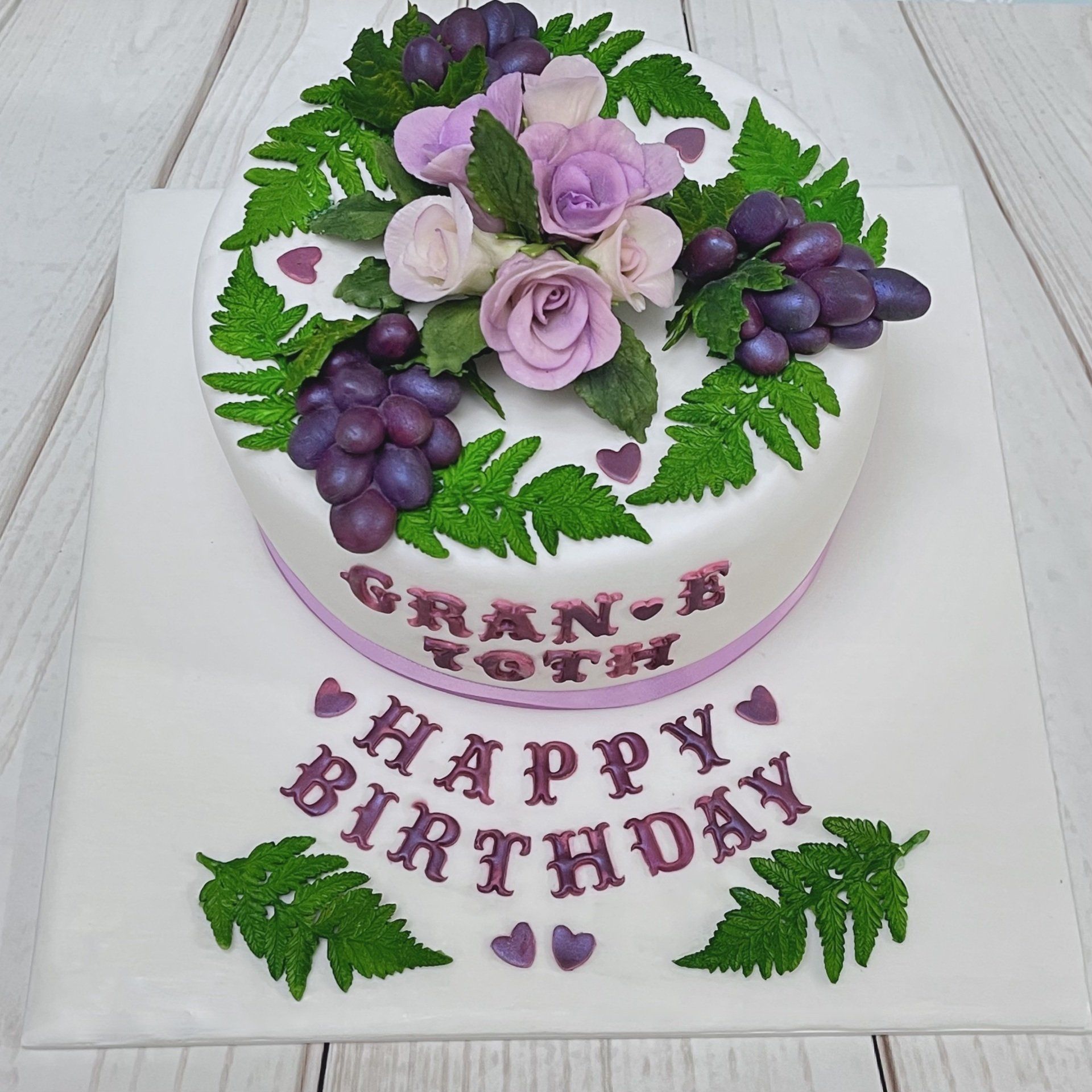 70th Birthday cake with white fondant, mauve sugar roses, sugar purple grapes, sugar fern leaves, purple fondant hearts and purple writting.