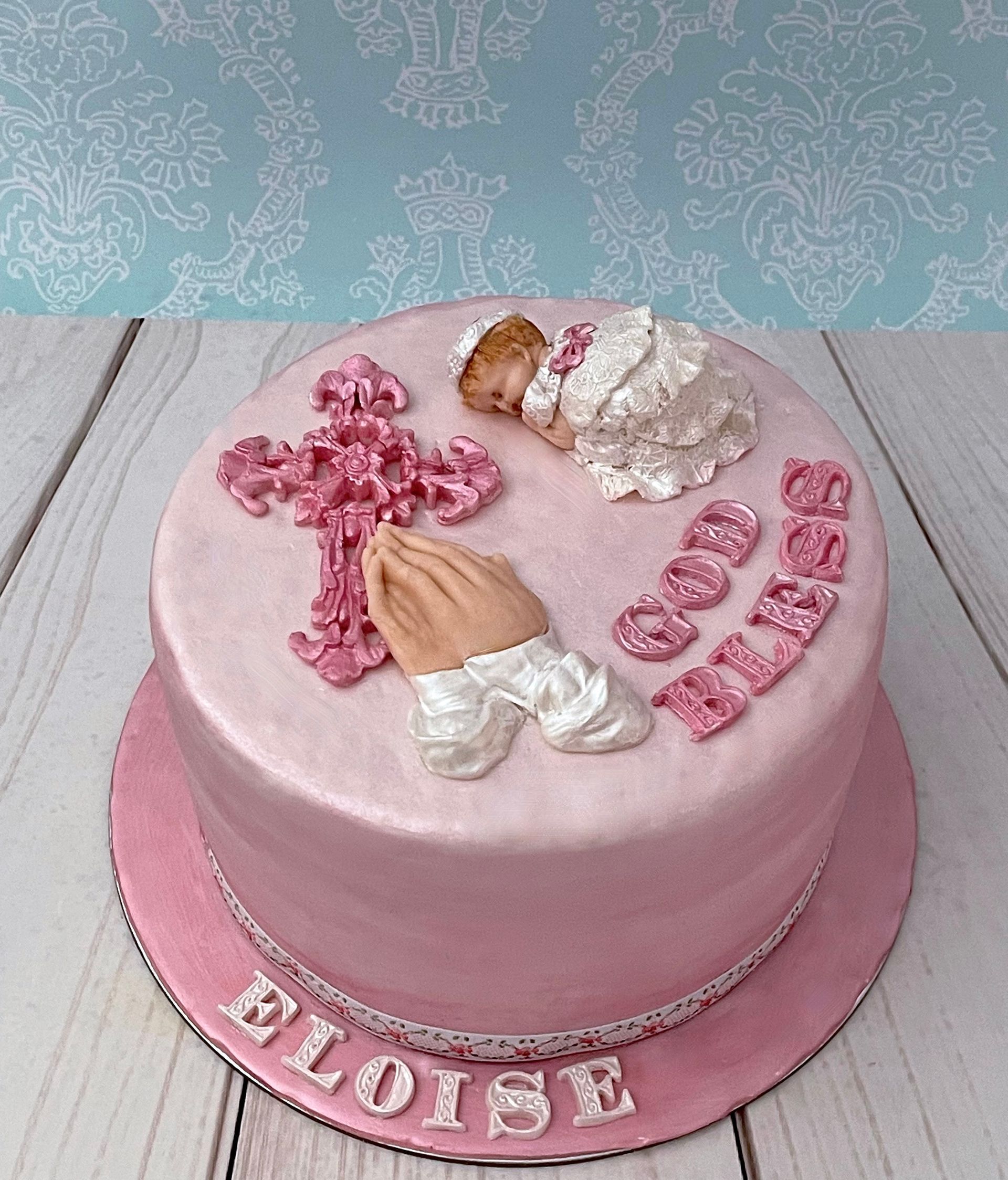 Pink Christening cake with Fondant Cross, Fondant Baby girl in a white fondant dress, Fondant praying hands and fondant 