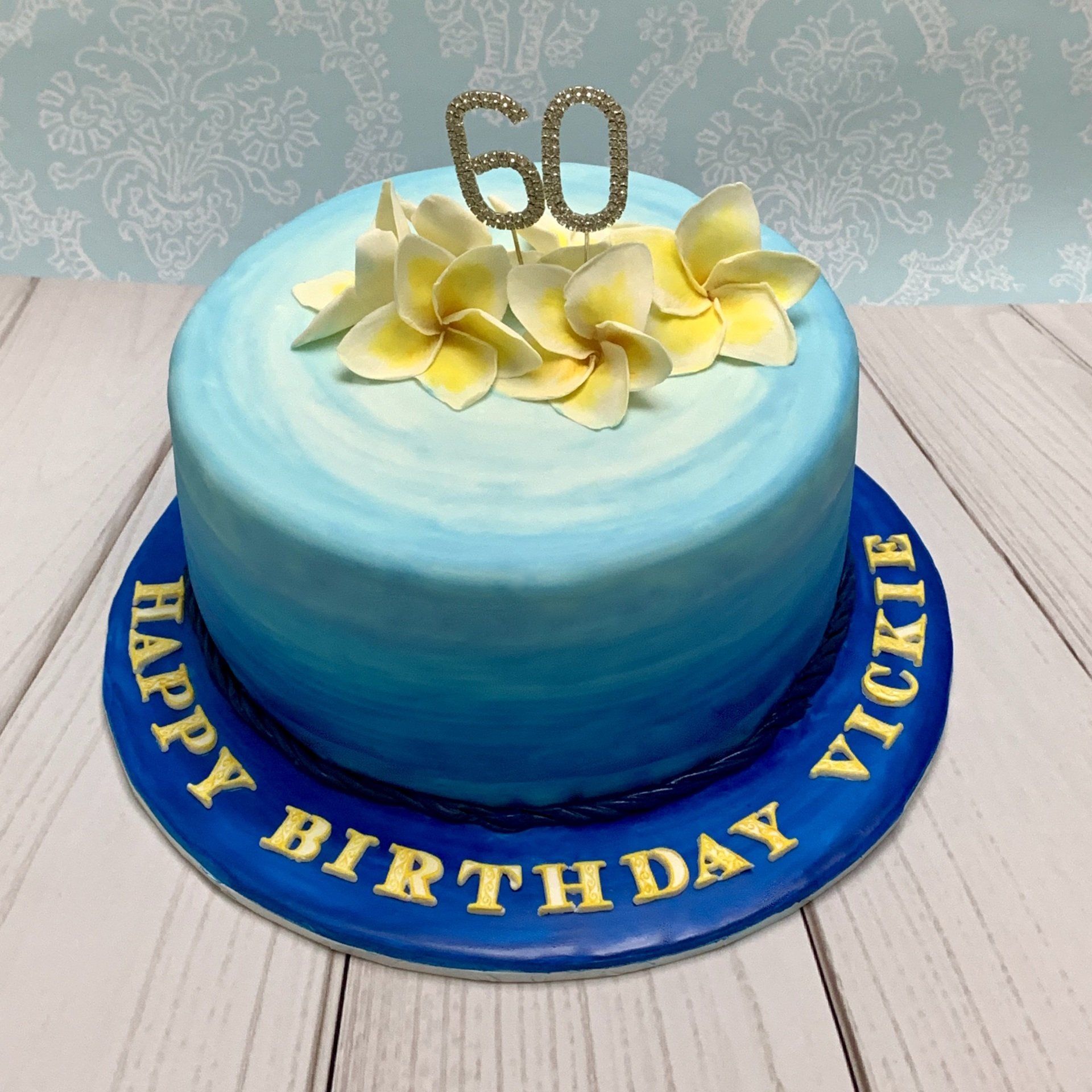 Ombre Blue Birthday cake with Diamante 60, handmade sugar frangipani flowers and writing of the board..
