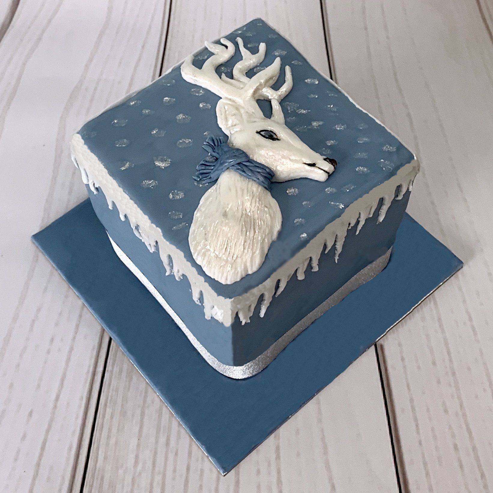 Square Christmas cake with soft wedgwood blue fondant, white moulded fondant reindeer, and fondant snow.