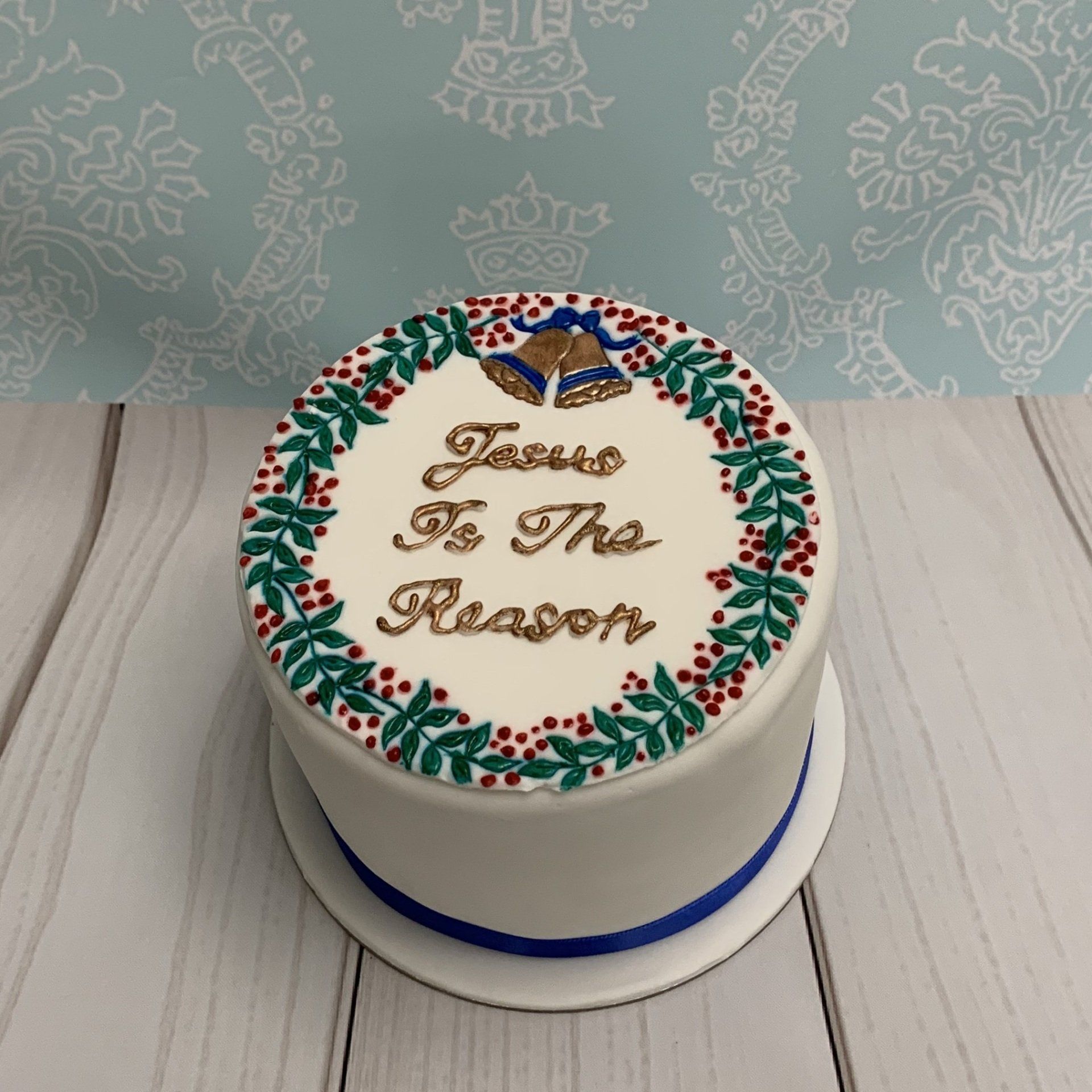 Round Christmas cake With stamped and piped details Bells, Holly and the words Jesus in the reason.