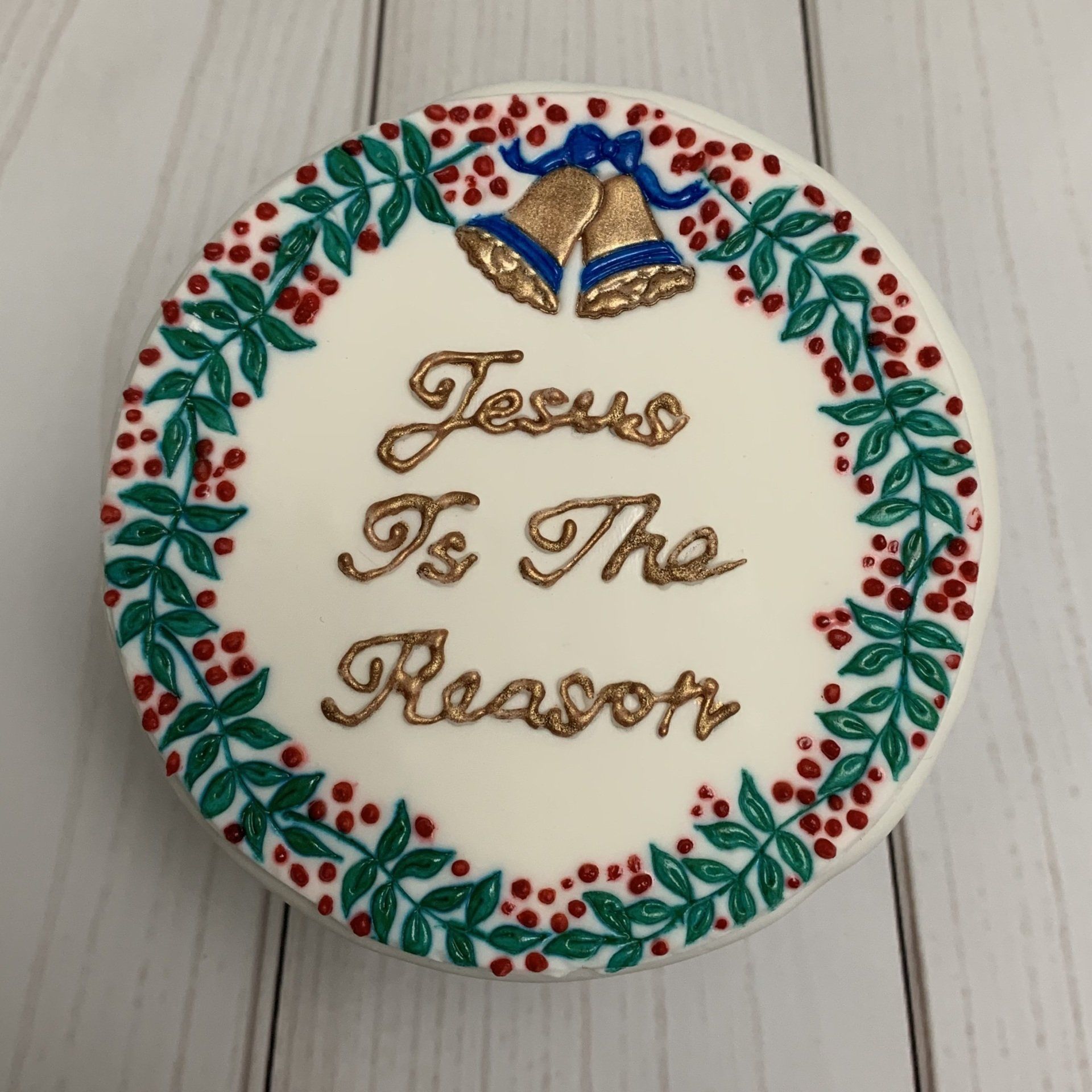 Round Christmas cake With stamped and piped details Bells, Holly and the words Jesus in the reason. Close up of top