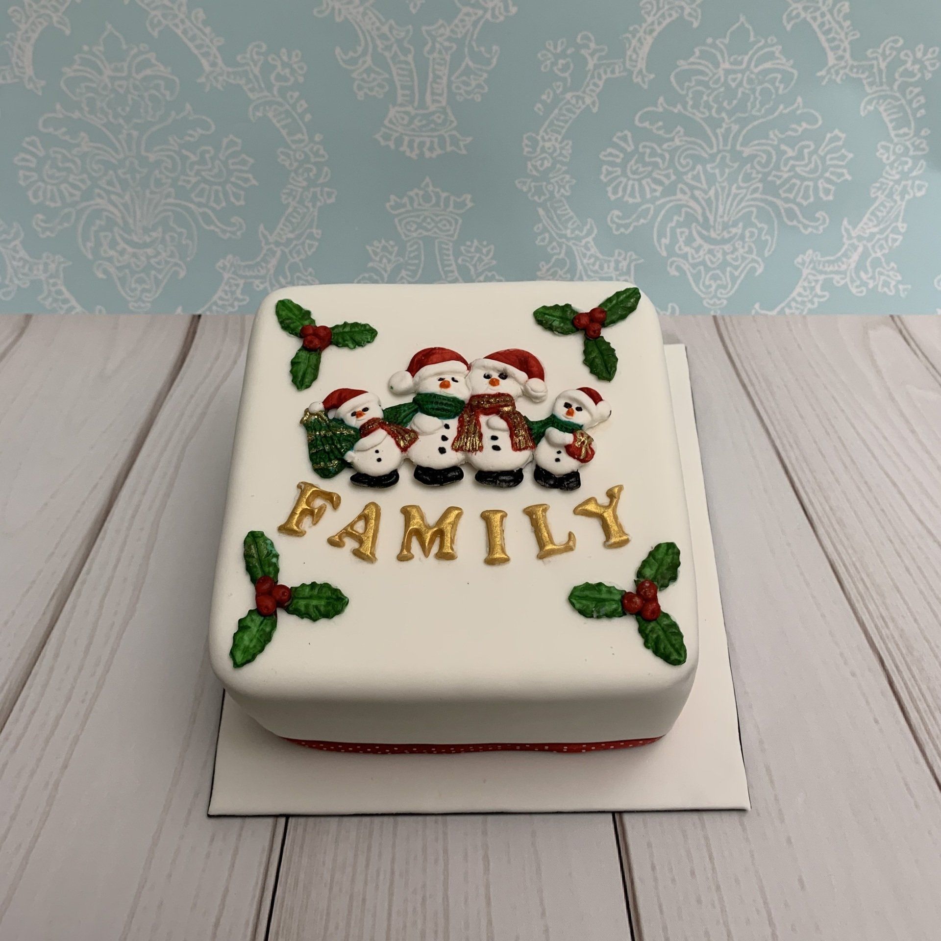 Square Christmas cake with snowmen, holly and the word family.