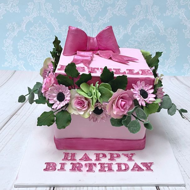 Pink Flower Box  Cake with sugar roses, sugar daisies Sugar hydrangeas and sugar eucalyptus leaves. And Happy Birthday and the birthday name.