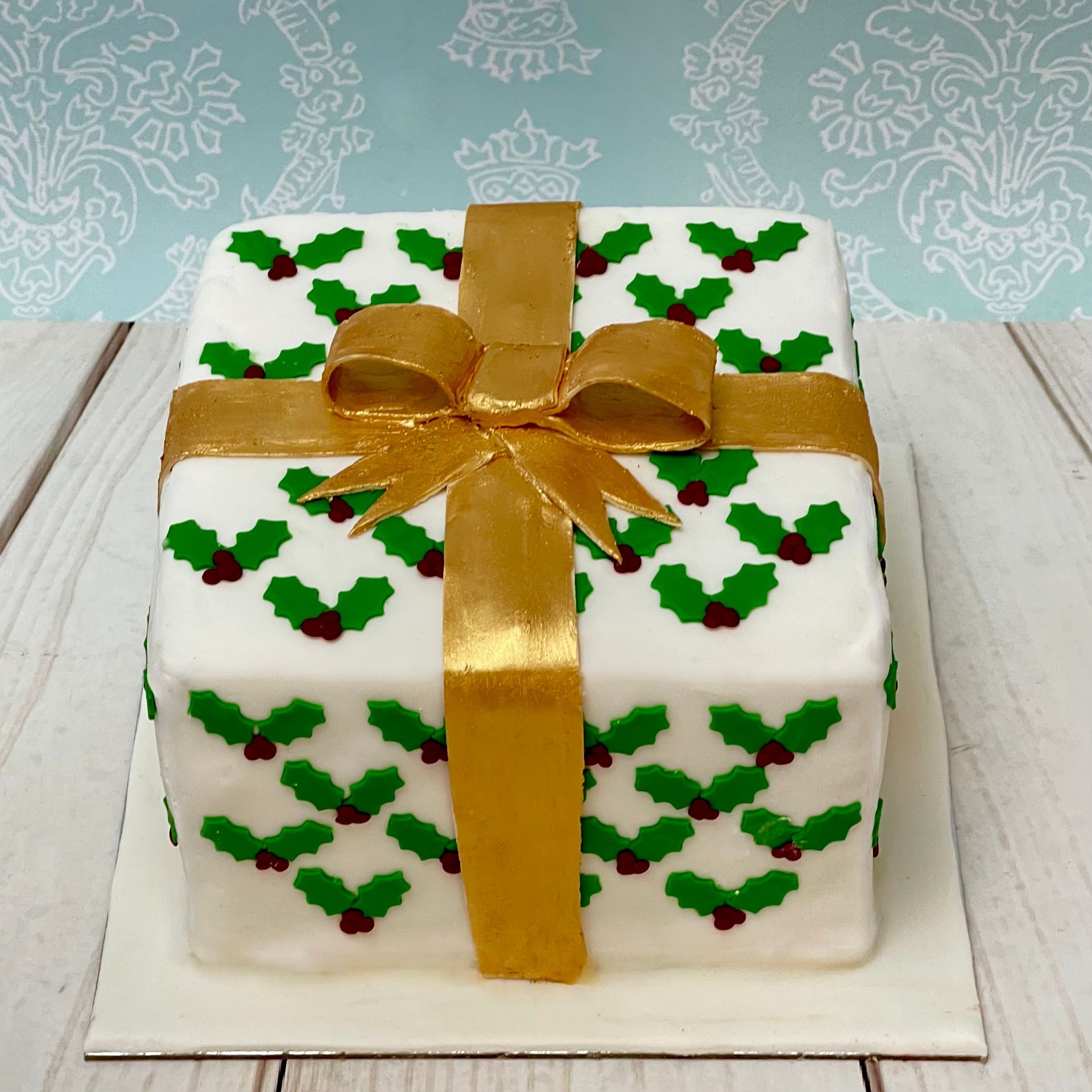 Christmas cake covered in fondant decorated to look like a Christmas present with fondant holly and gold fondant ribbon. 