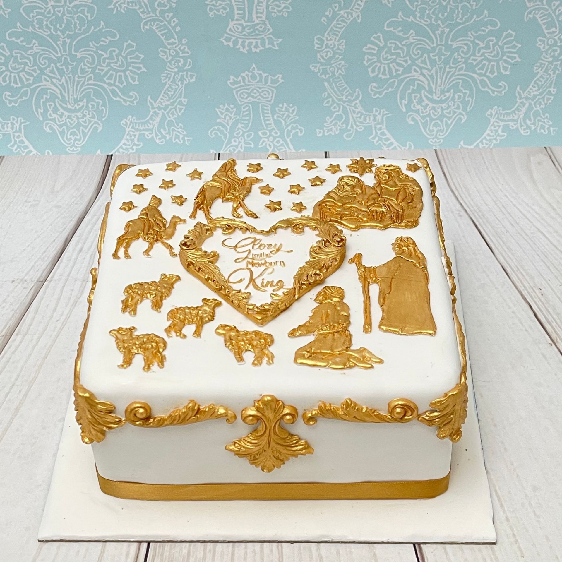 Christmas cake covered in fondant with gold fondant filigree moldings, gold fondant nativity scene and hand painted gold Glory to the New Born King Heart.