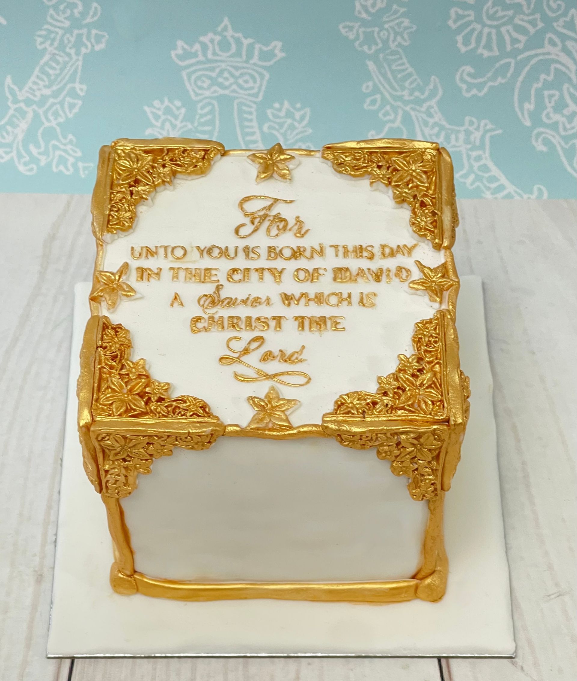 Christmas cake covered in fondant with gold fondant filigree moldings and hand painted gold Christian Christmas sentiments. 