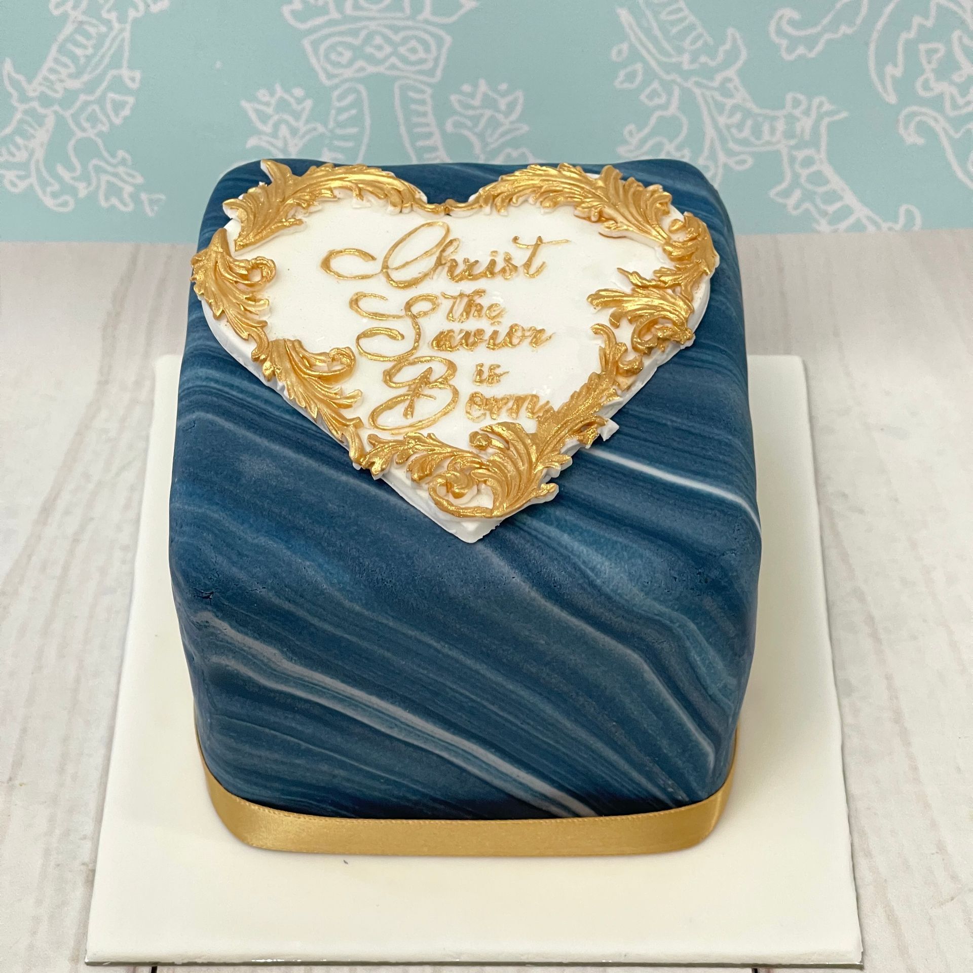 Christmas cake covered in marbled Blue fondant with white fondant  heart and gold Christ the Saviour is born 