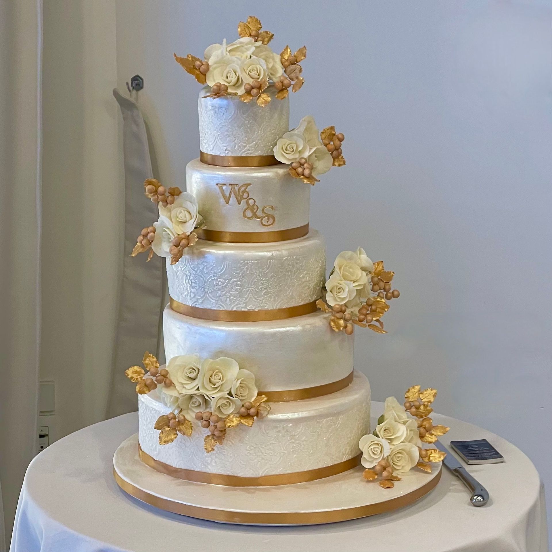 5 Tiered Wedding Cake Sails Resort Port Macquarie. Pearl White textured tiers, Trimmed wth Gold Ribbon and Decorated with lots of Handmade White Sugar Roses, Gold Sugar Leaves and Gold Sugar Berries.