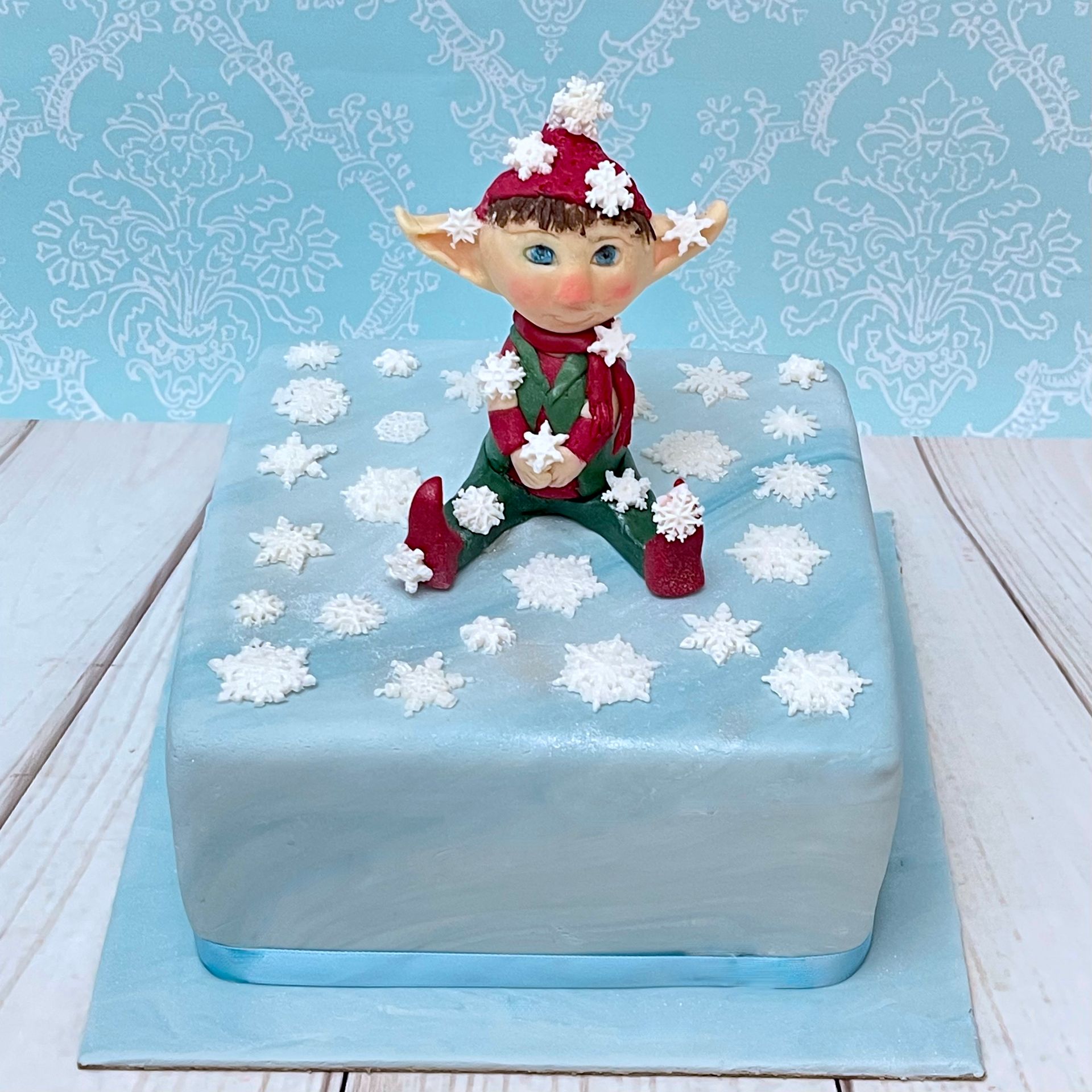 Christmas Cake covered in soft blue fondant and decorated with fondant snowflakes and a cute hand sculpted fondant Christmas Elf.
