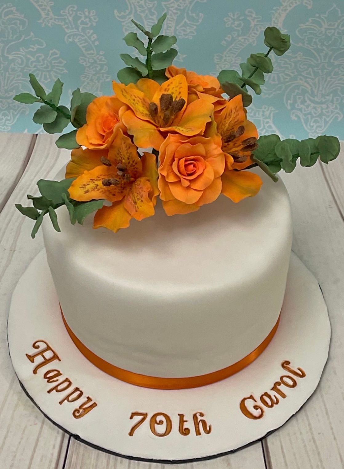White Fondant Birthday Cake with Orange sugar flowers and sugar eucalyptus leaves.