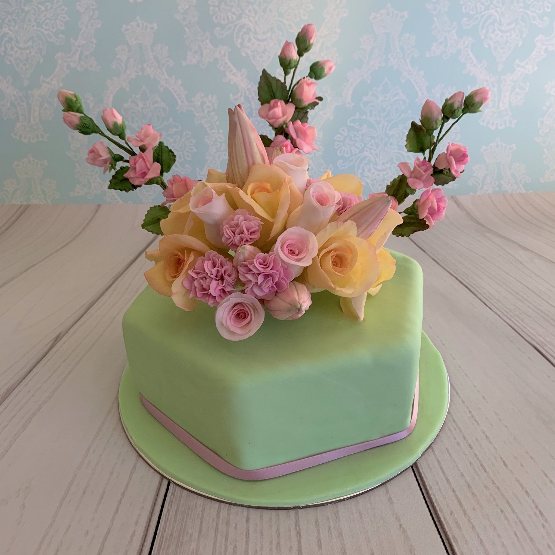 Hexagonal cake with soft green fondant and lots of beautiful sugar flowers in soft pink, soft yellow and soft apricot colours.