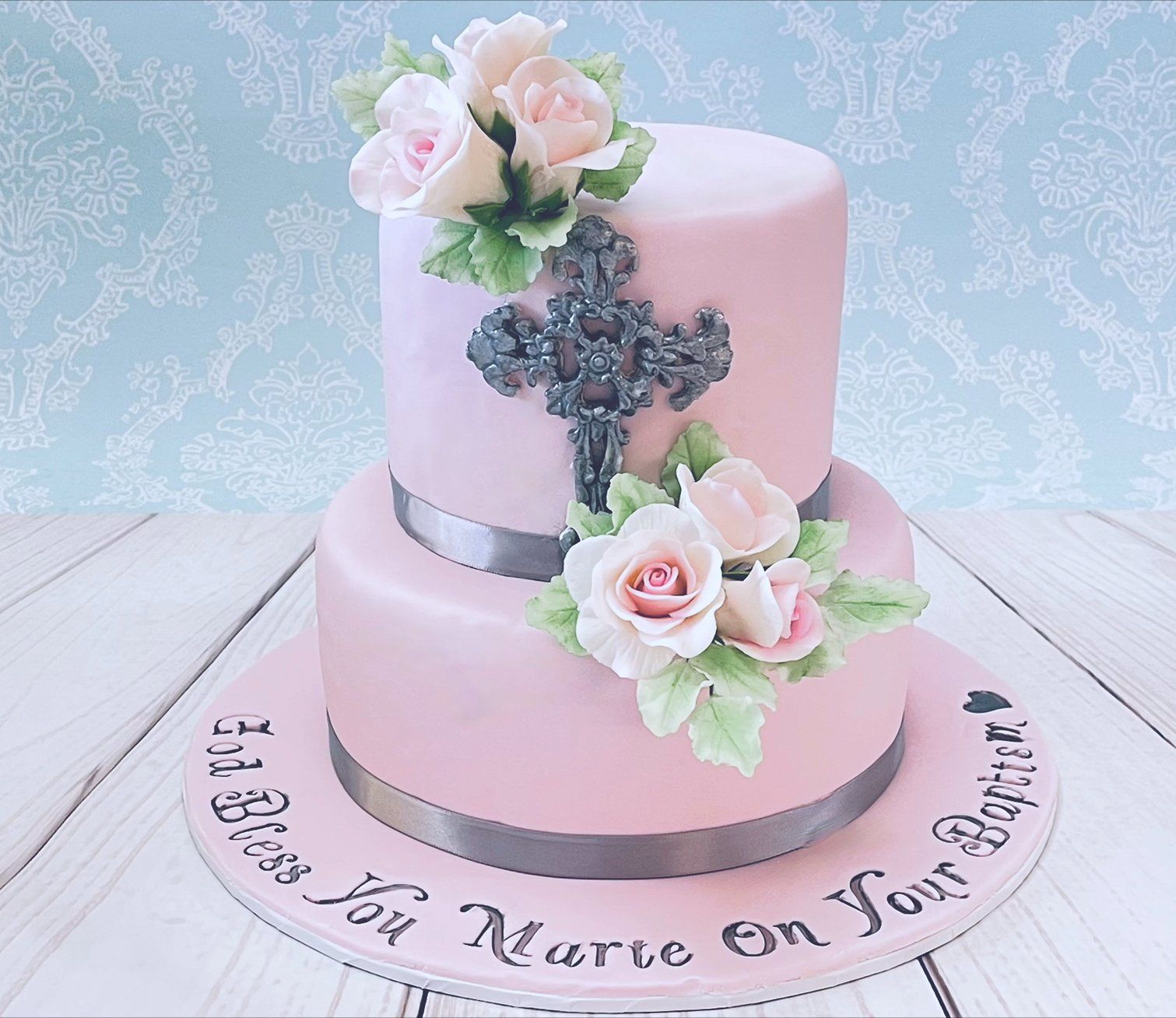 Ladies Baptism Cake. Two tier with soft pink fondant, silver ribbon, ornate silver fondant cross, silver hand writting and pastel sugar flowers.
