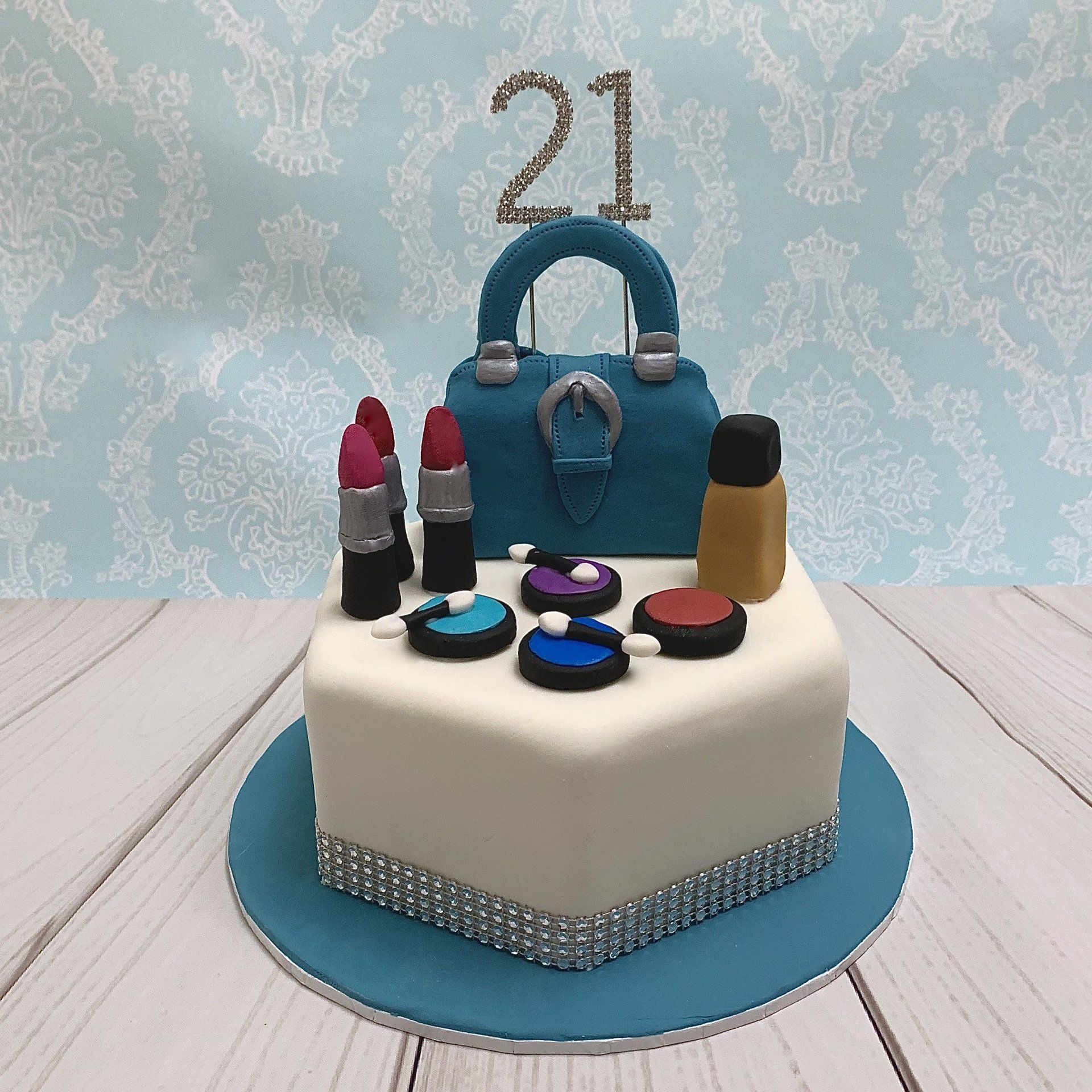 Hexagon cake with white fondant Diamanté 21 and trim. A hand sculpted blue fondant purse with silver fondant buckle detail and hand sculpted fondant make up. on a blue fondant board.