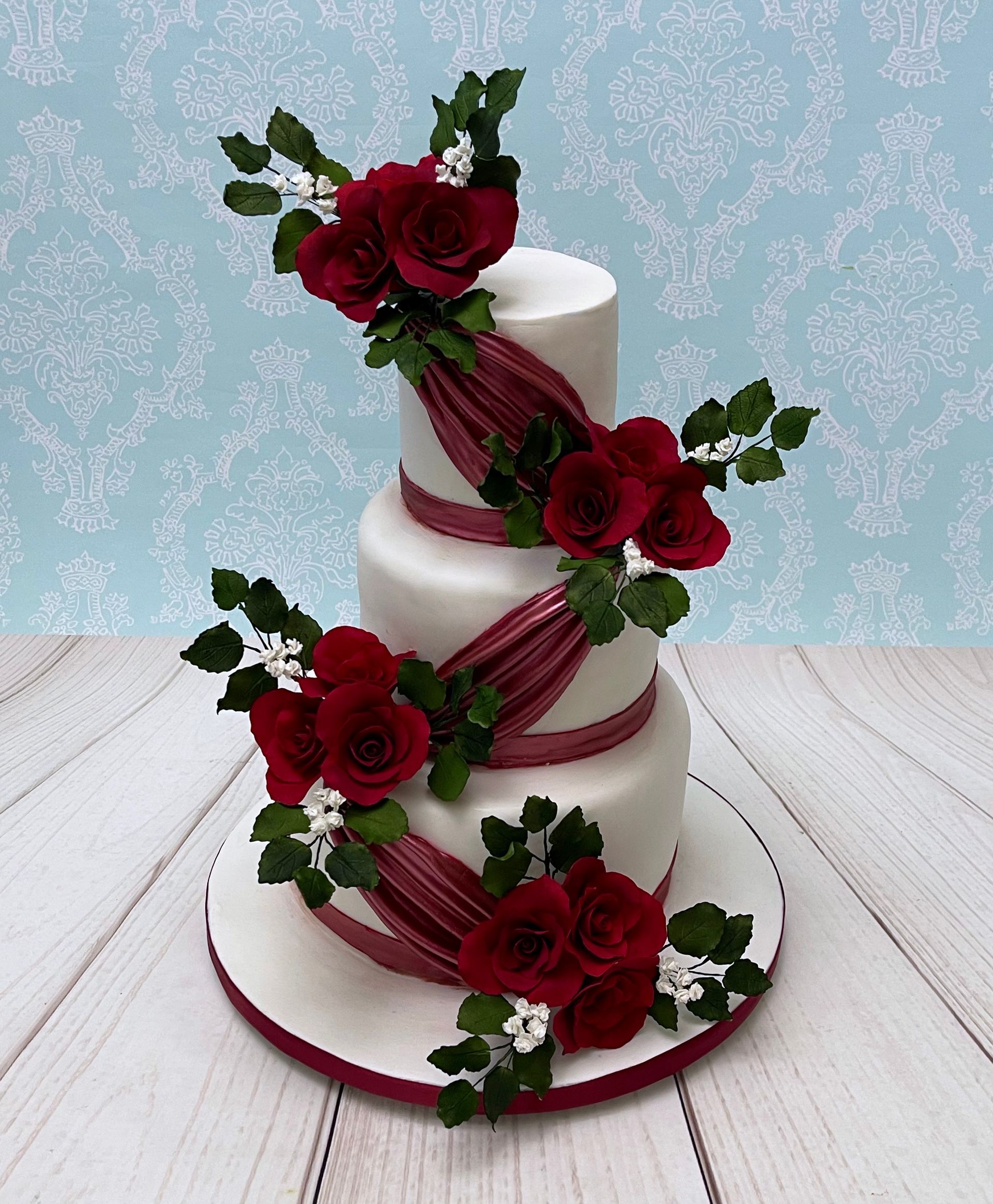 3 tiered Wedding Cake with burgundy sugar roses, green sugar rose leaves, white sugar babies breath and burgundy fondant drapes