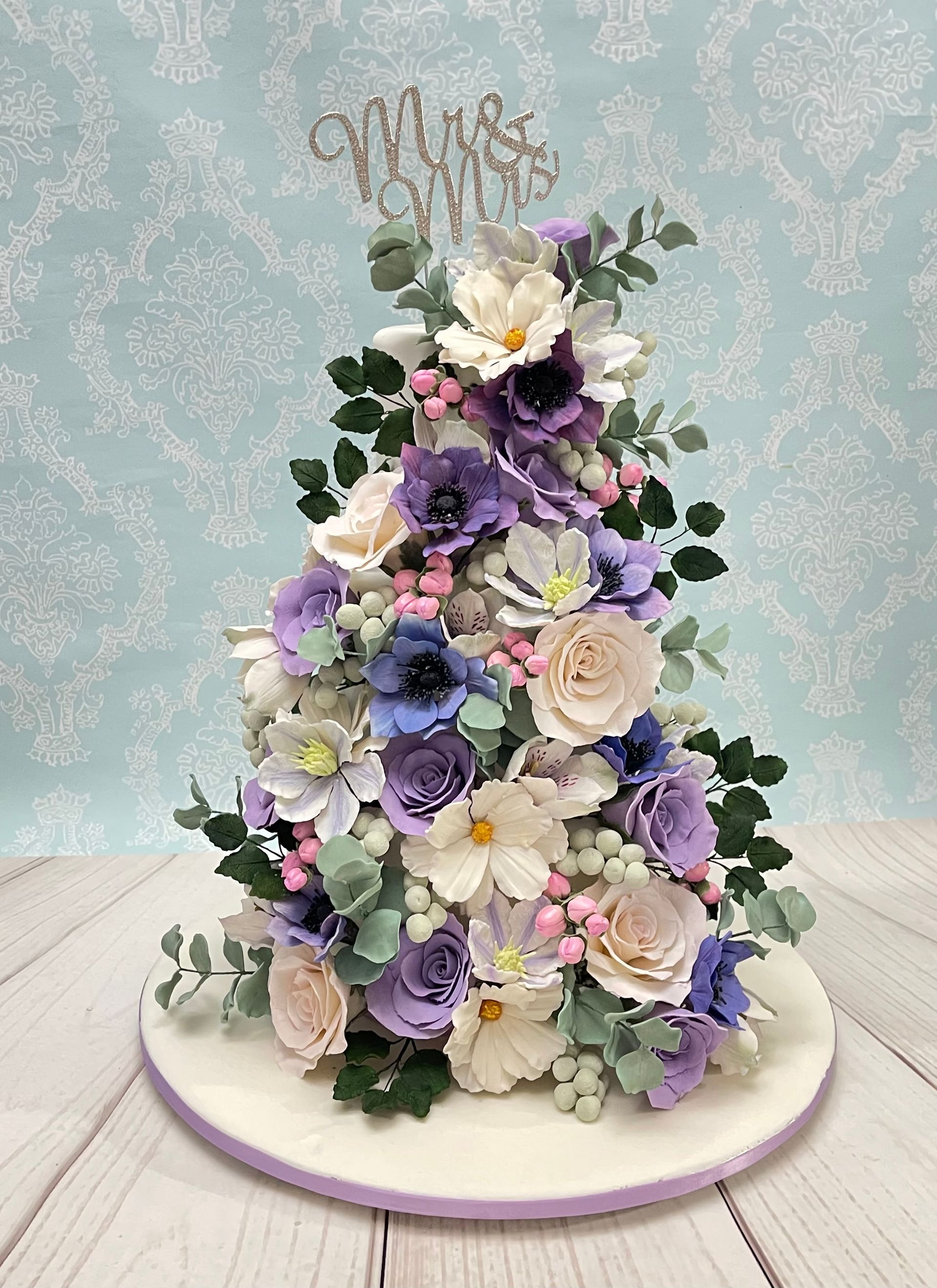 Gorgeous Wedding Cake Port Macquarie. White fondant, Mauve Ribbon Trim, Diamanté Mr & Mrs Topper and Cascading White and shades of Mauve Sugar Flowers.