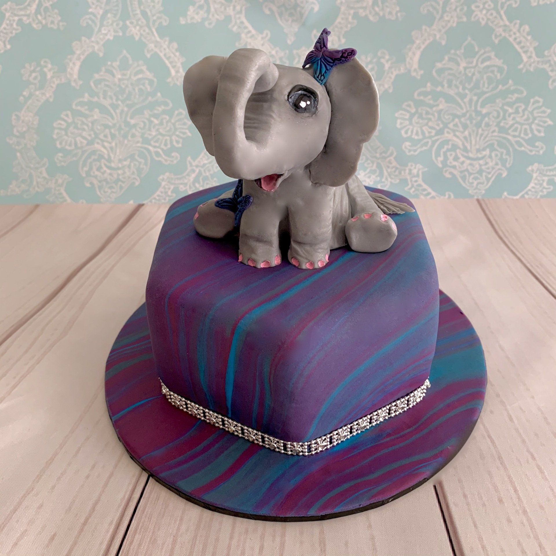 Birthday cake with bright purple, pink and blue, marbled fondant. With a very cute hand sculpted fondant elephant on top.