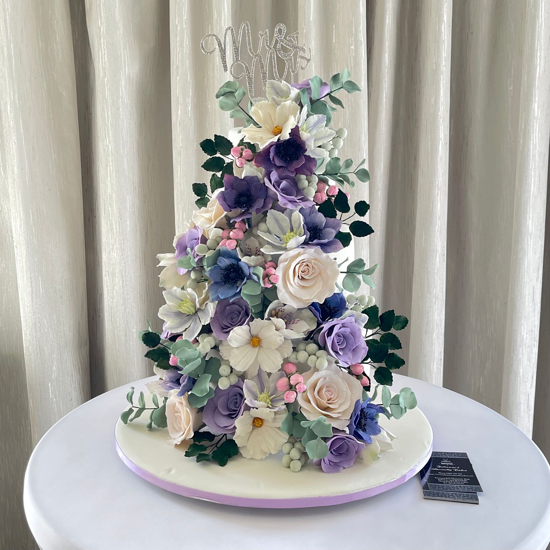 Gorgeous Wedding Cake Port Macquarie. White fondant, Mauve Ribbon Trim, Diamanté Mr & Mrs Topper and Cascading White and shades of Mauve Sugar Flowers.