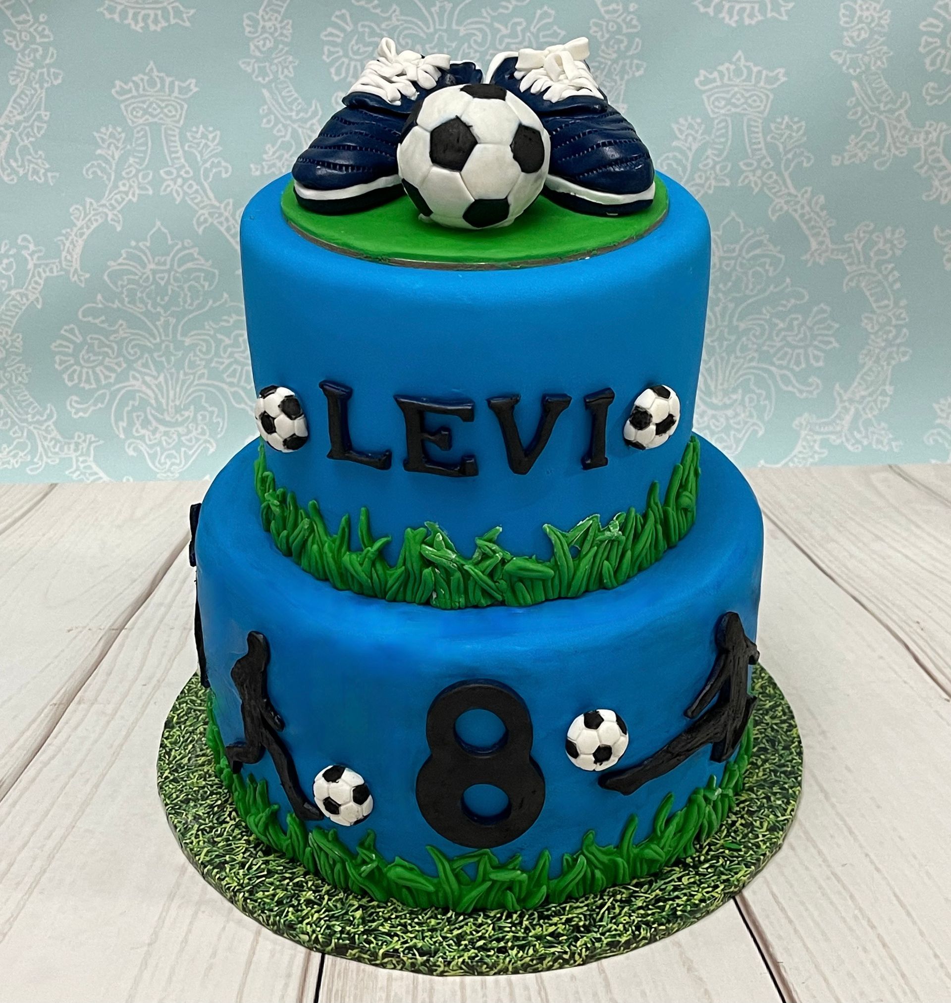 Soccer themed cake with hand sculpted soccer shoes, soccer ball, and soccer silhouettes. 