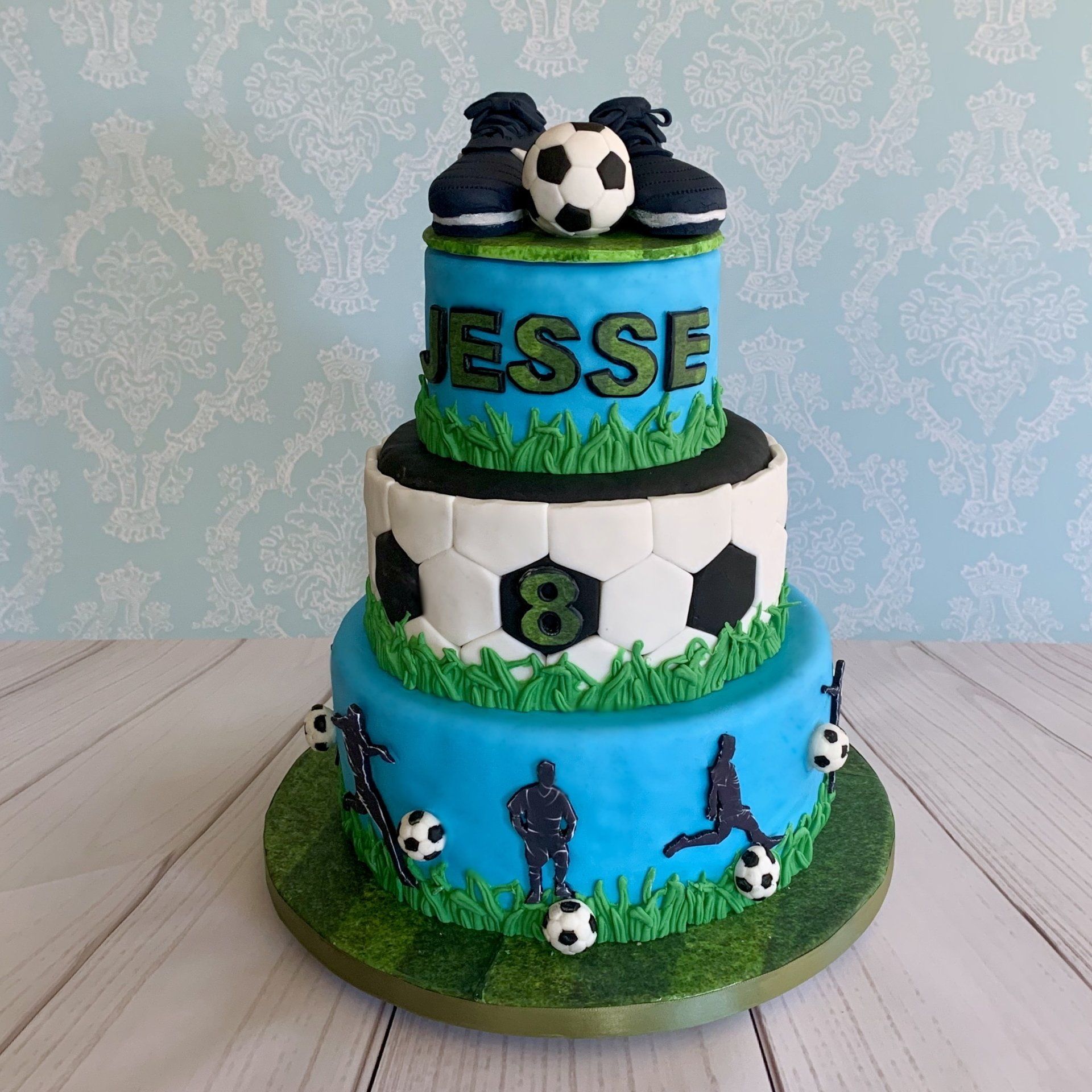 Three tiered Soccer themed cake with hand sculpted soccer shoes, soccer ball, soccer silhouettes and other soccer elements.