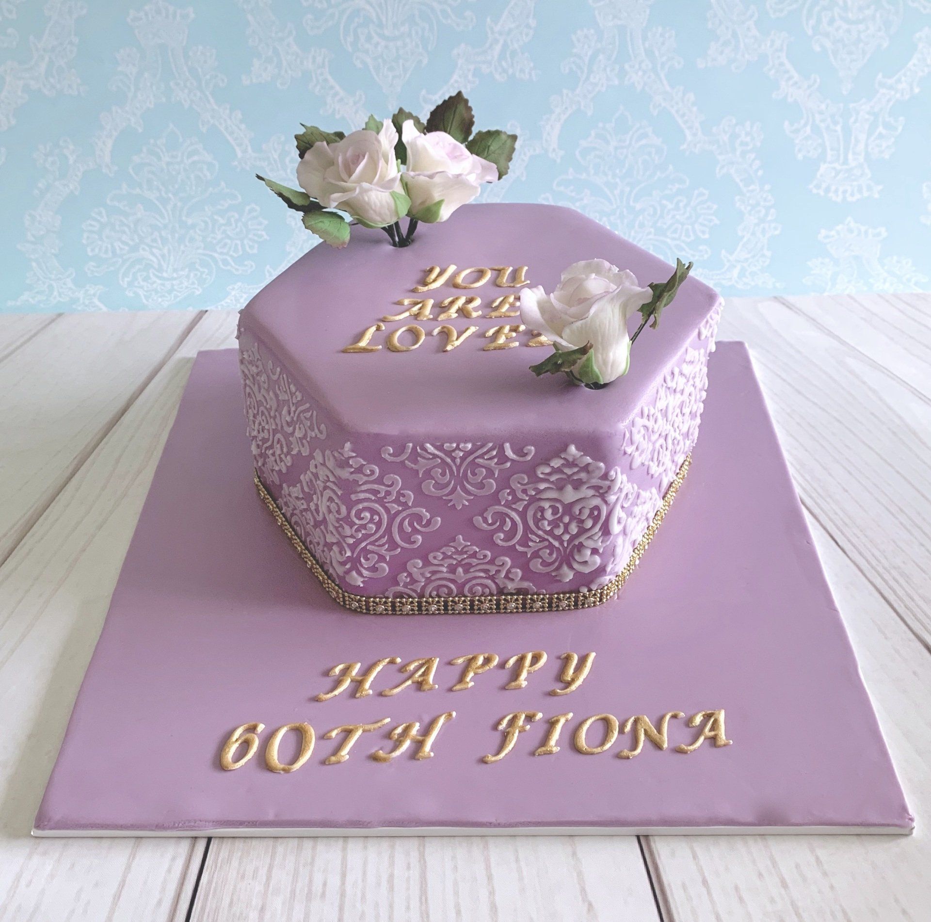 Soft mauve fondant, with hand made white and mauve sugar roses, sugar rose leaves, on gold writting 
