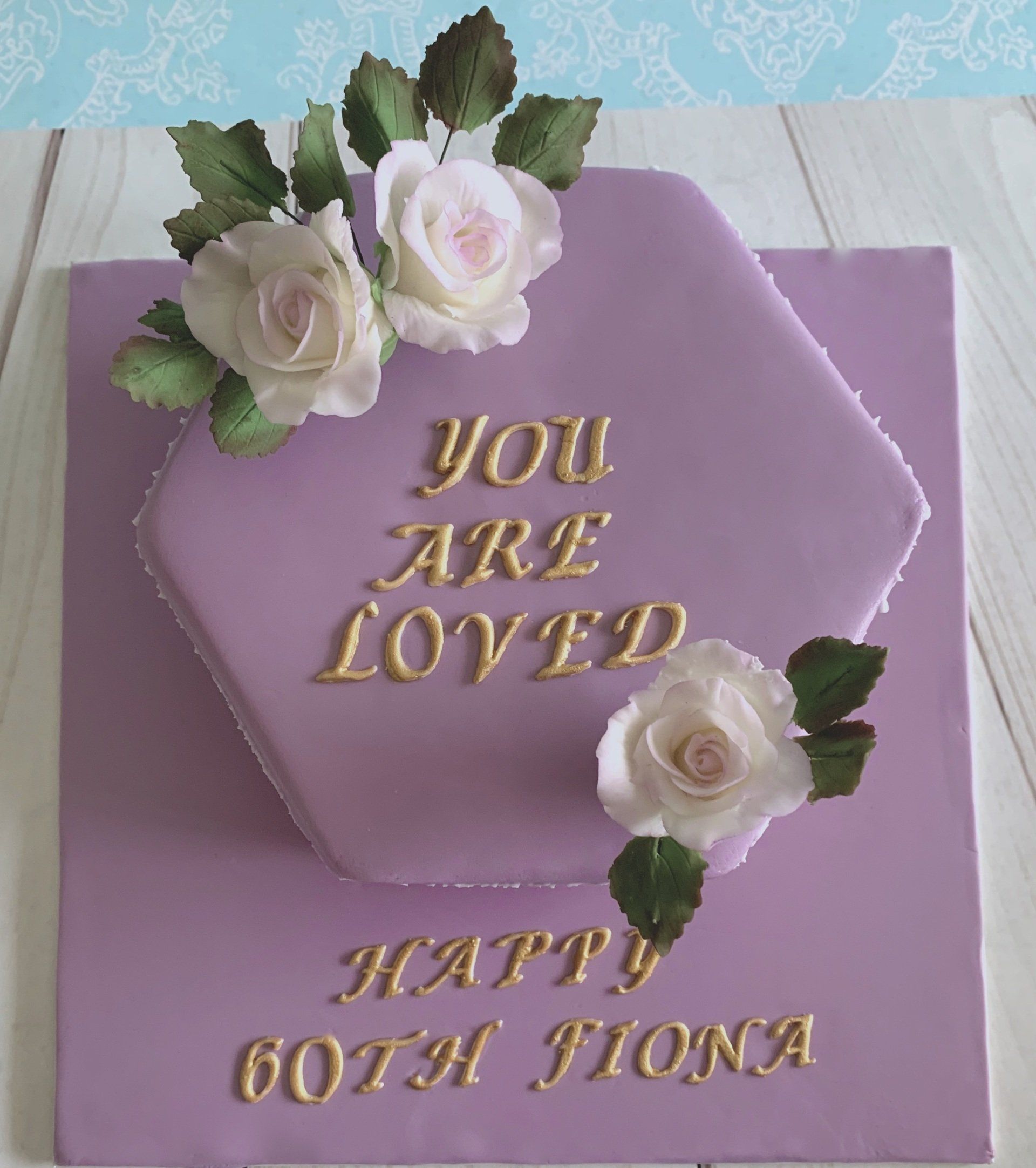 Soft mauve fondant, with hand made white and mauve sugar roses, sugar rose leaves, on gold writting 