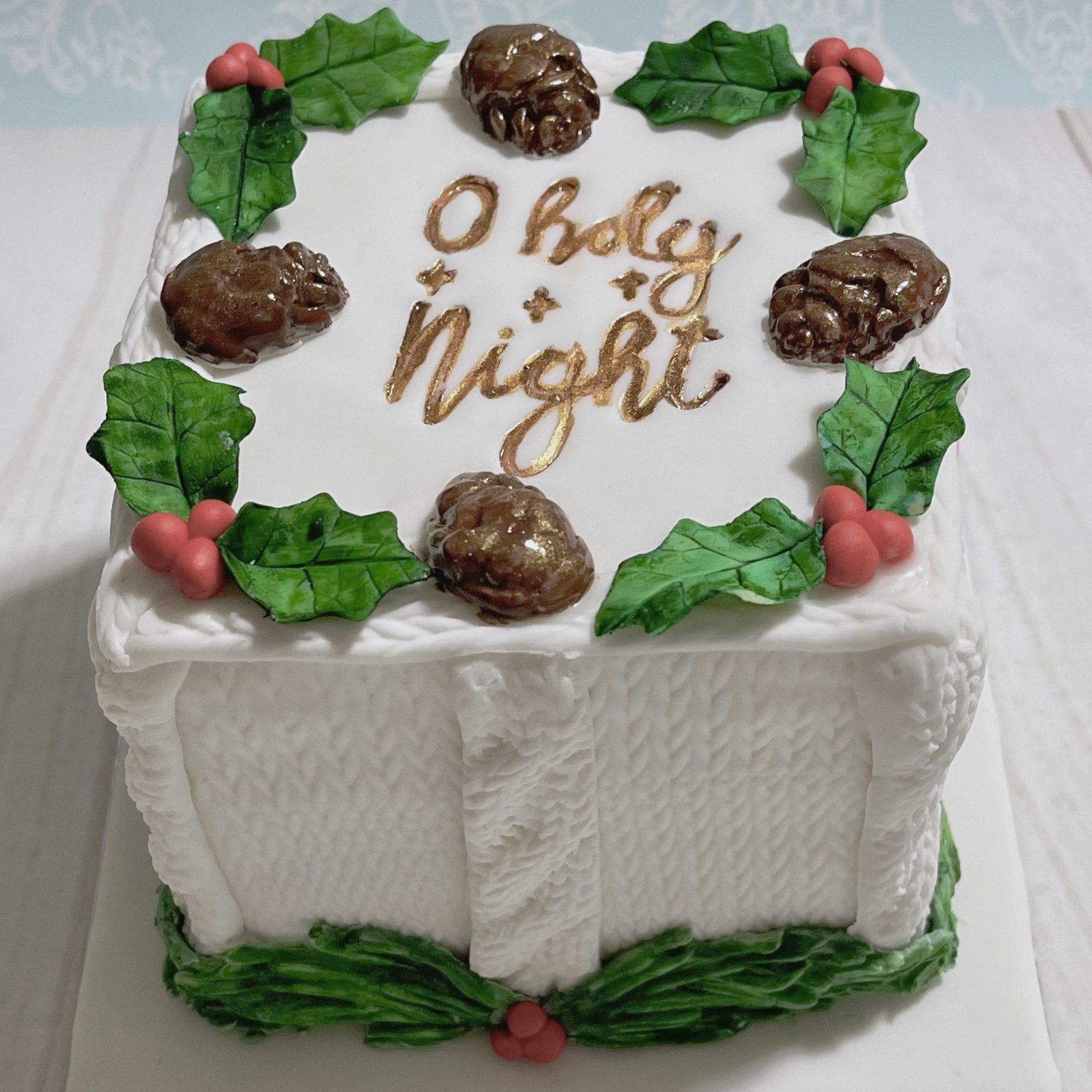 Christmas cake with Fondant Holly, Fondant mini pinecones, fondant knitted effect on the sides, and the words O Holy Night