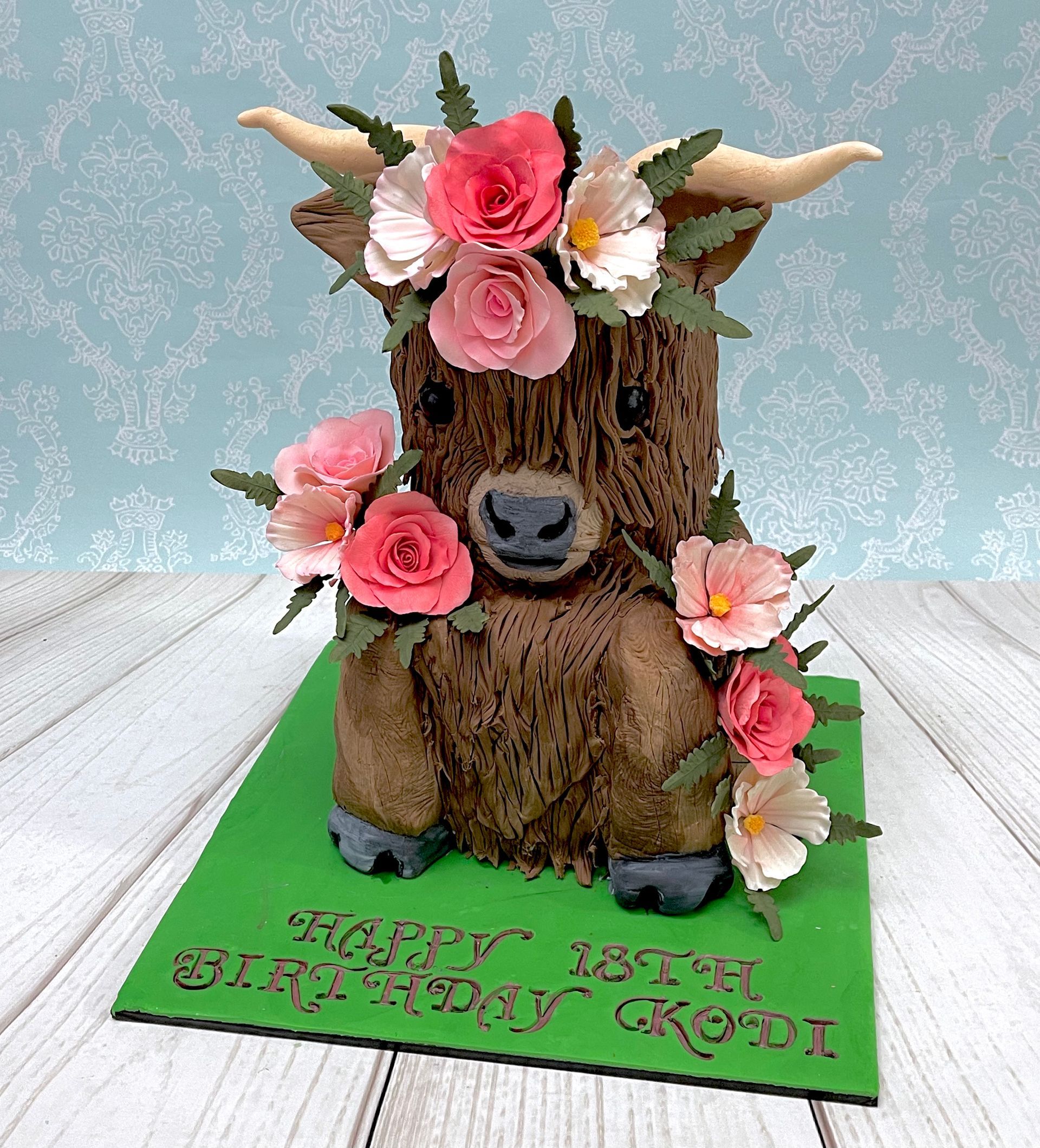 Cute Two Tier Highland Cow Cake With Pink White and Apricot Sugar Flowers, and sugar Leaves. 18th Birthday Port Macquarie.
