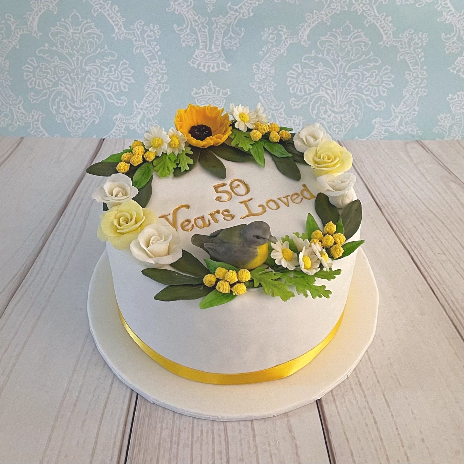 Golden Wedding Anniversary cake with a handsculpted little yellow robin, Handmade sugar flowers in whites and yellows. And a hand painted gold 50 years loved