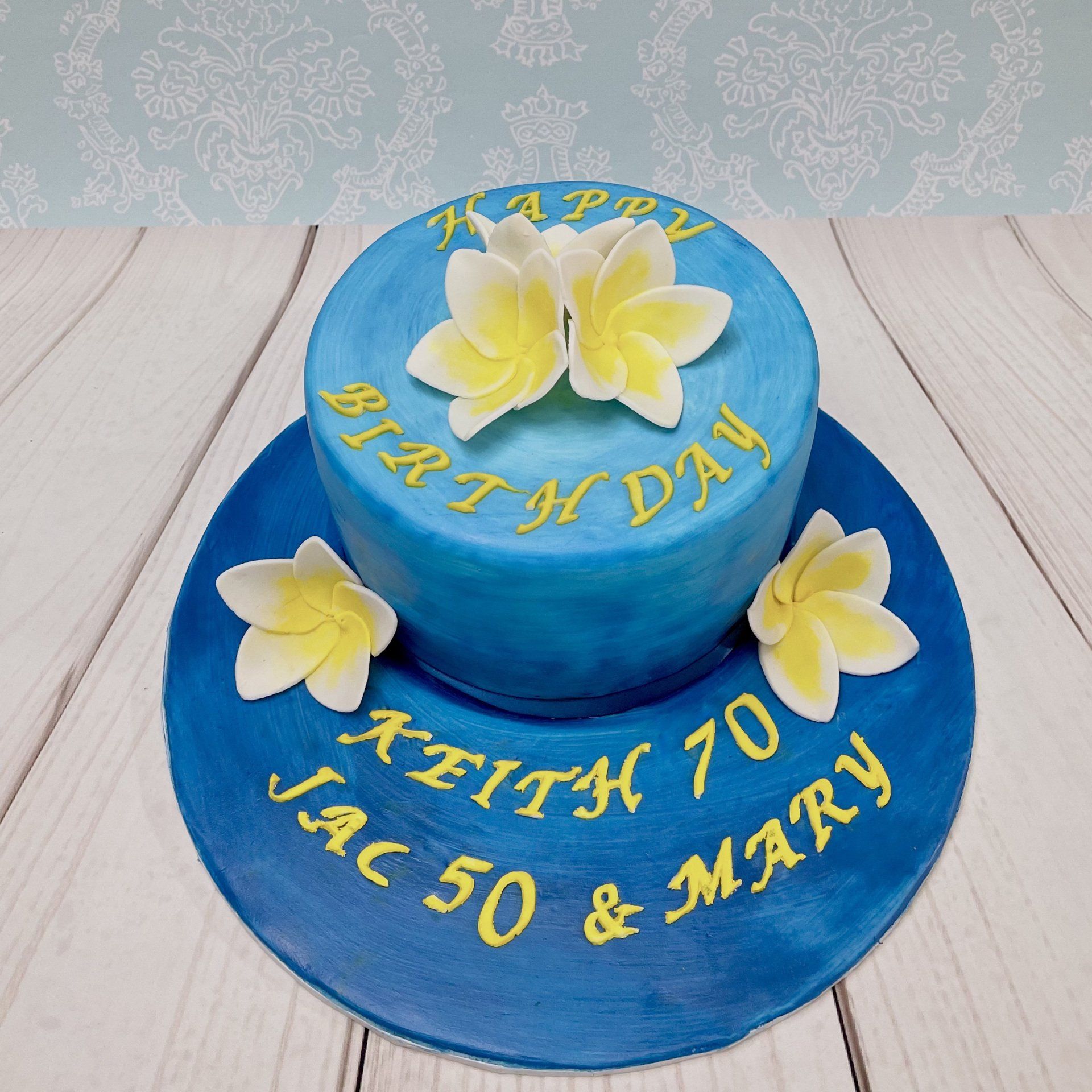Ombre Blue Birthday cake with handmade sugar frangipani flowers and writing of the board.